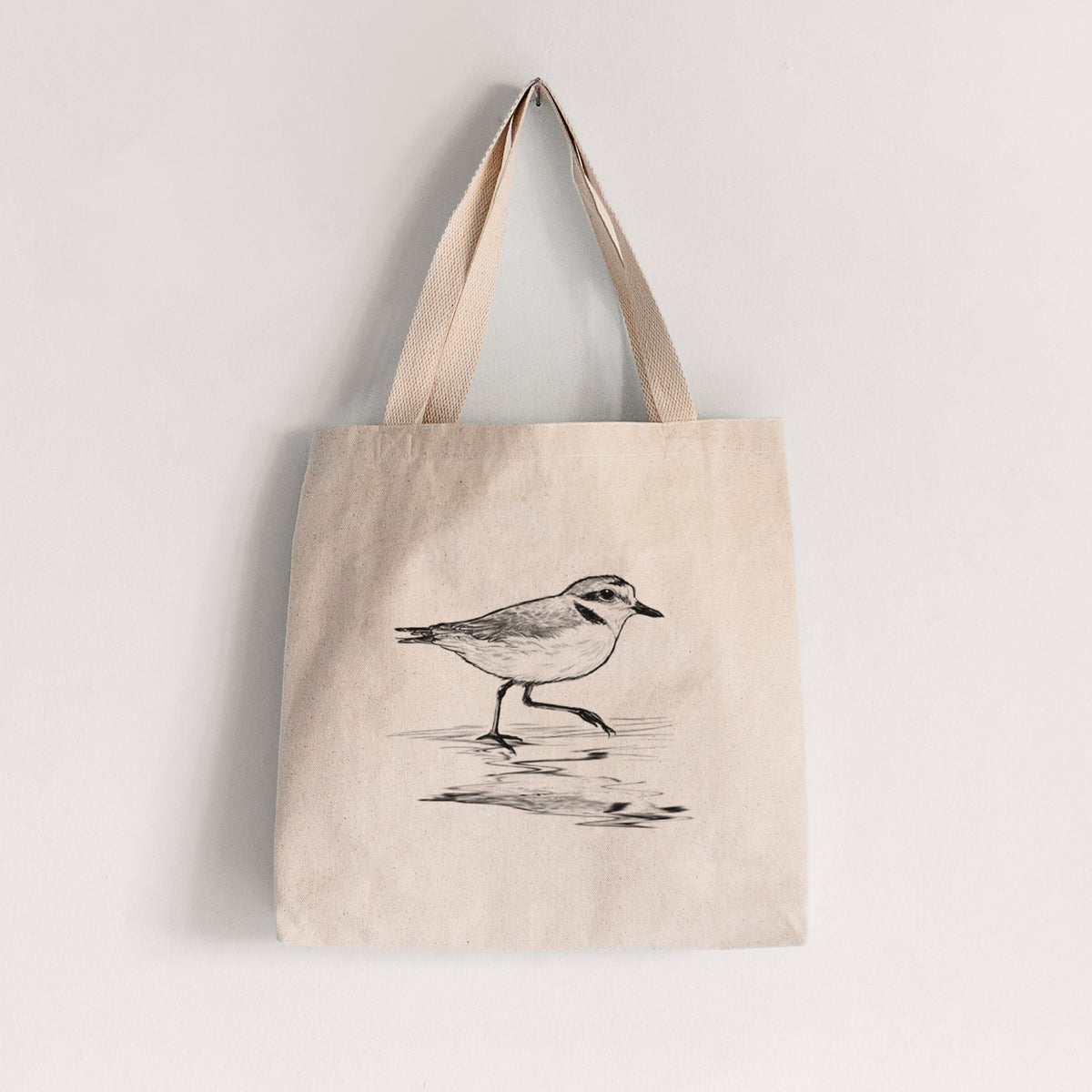 Natural canvas tote bag printed with a black ink sketch of a snowy plover running along the wet shoreline.
