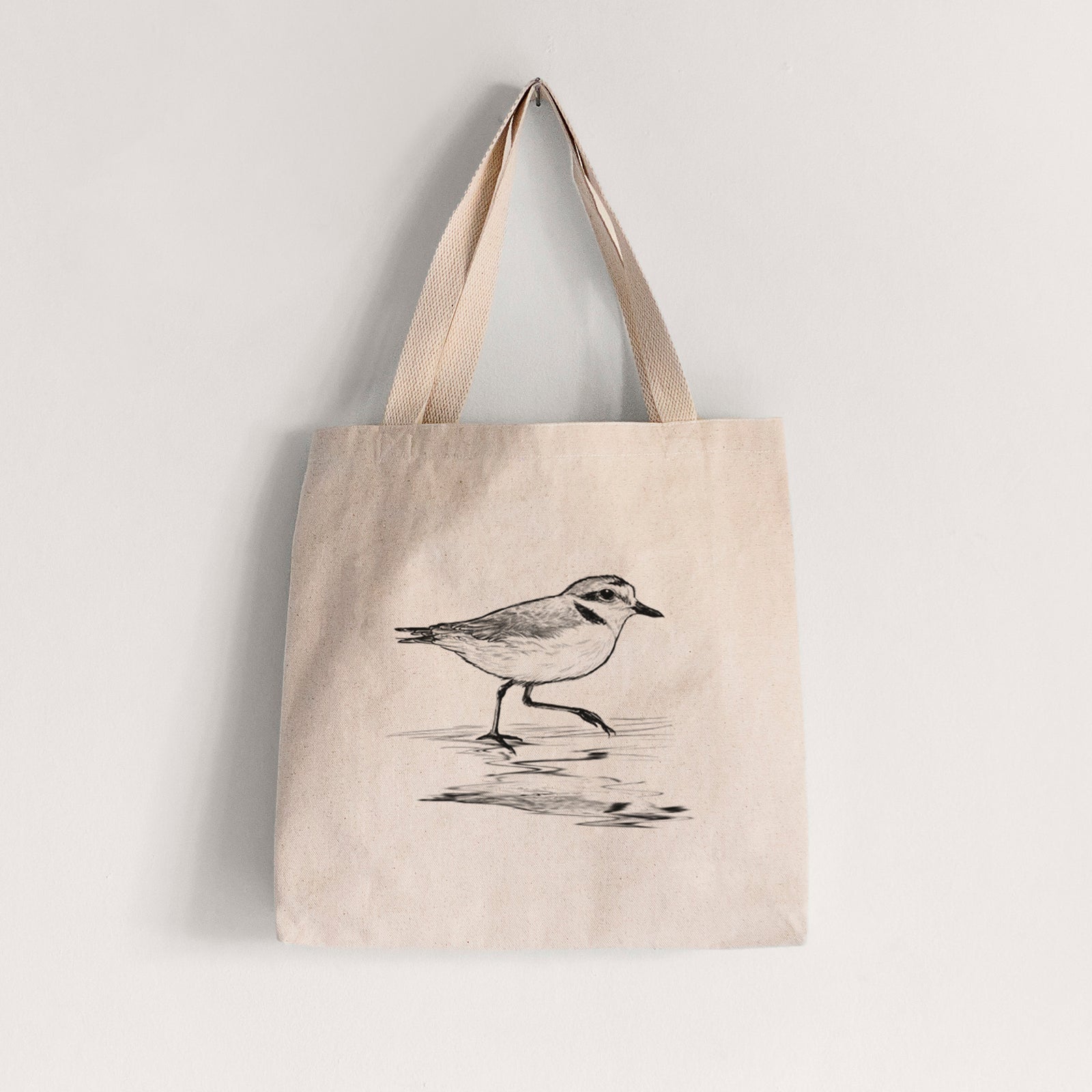 Natural canvas tote bag printed with a black ink sketch of a snowy plover running along the wet shoreline.