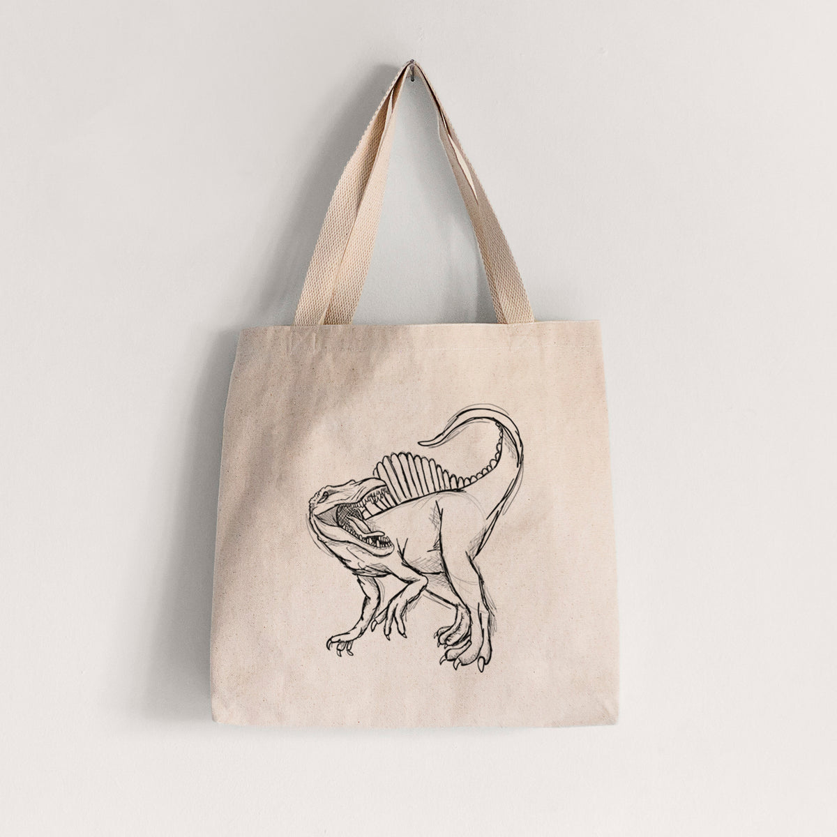 Natural canvas tote bag printed with a black ink illustration of a Spinosaurus with its tall sail-shaped back.