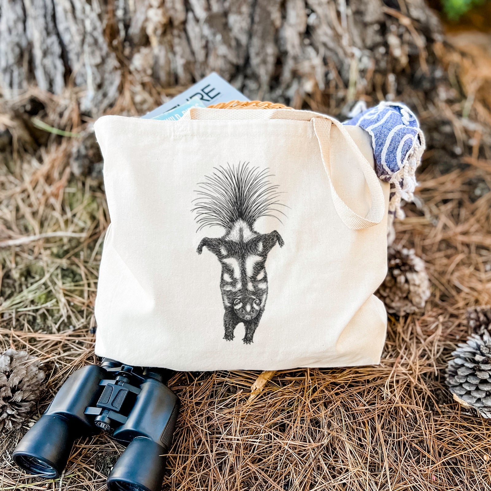 Natural canvas tote bag printed with a black ink illustration of a spotted skunk doing a handstand with its tail fanned.