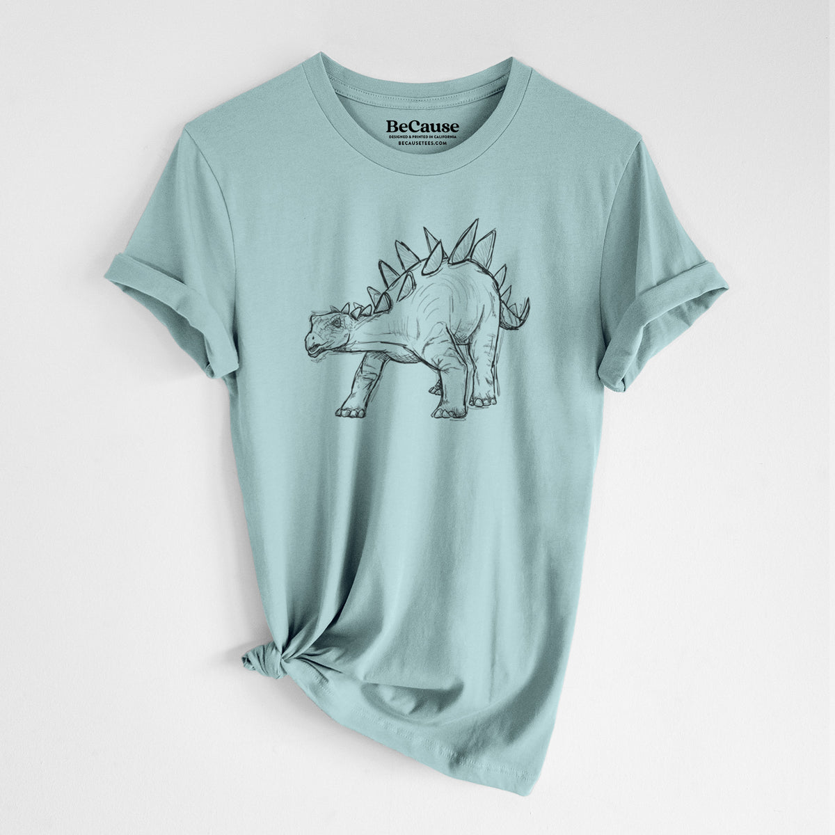 Dusty blue lightweight cotton t-shirt laid flat with the sleeves rolled, printed with a black ink illustration of a Stegosaurus with plates along its back.
