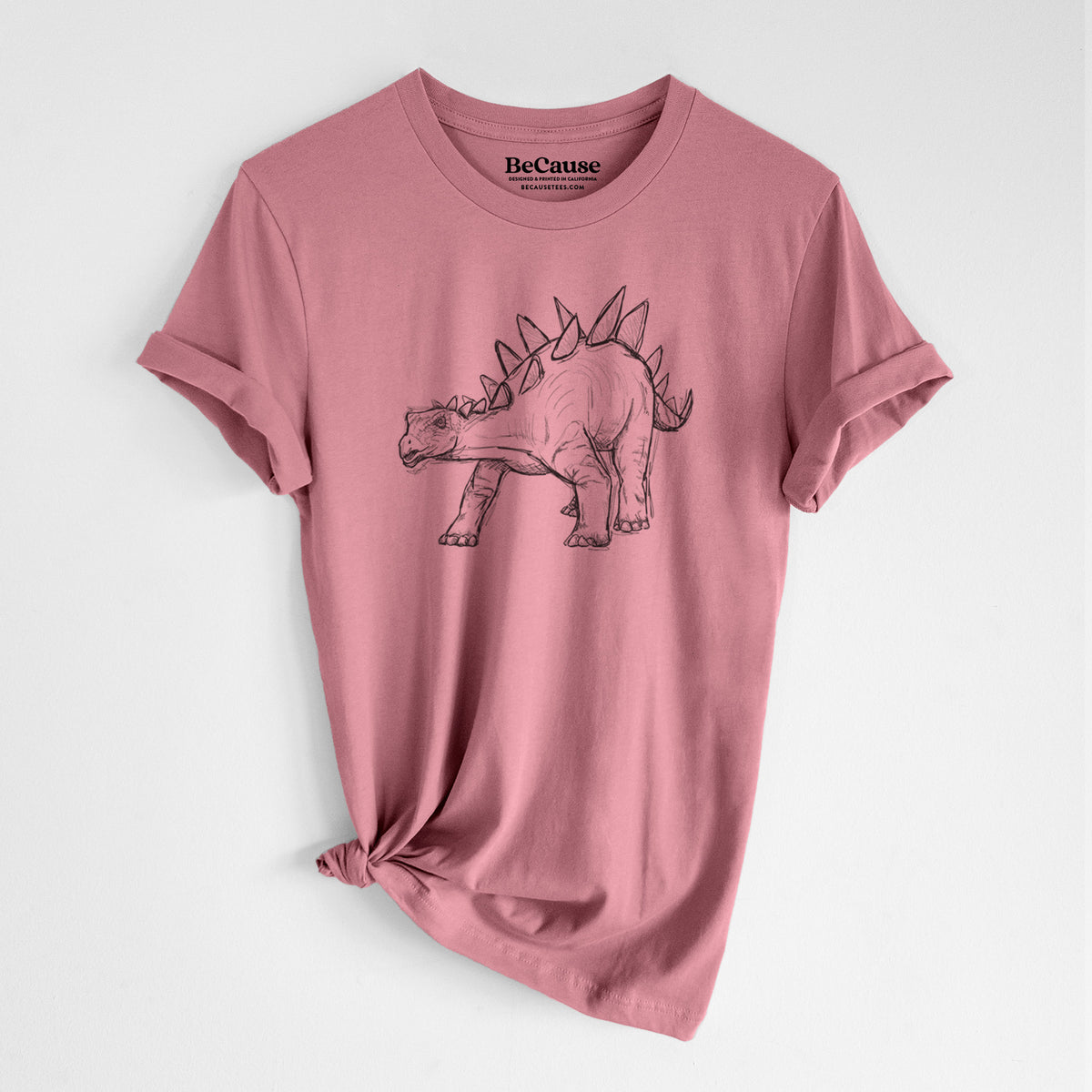 Mauve pink lightweight cotton t-shirt laid flat with the sleeves rolled, printed with a black ink illustration of a Stegosaurus with plates along its back.