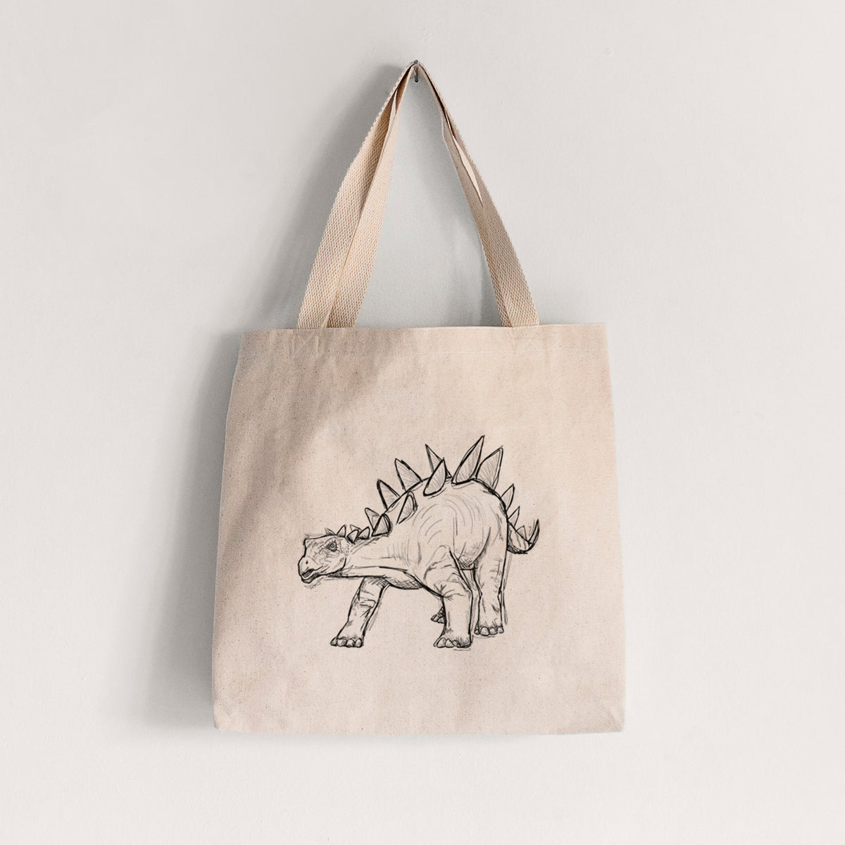 Natural canvas tote bag printed with a black ink illustration of a Stegosaurus with plates along its back.