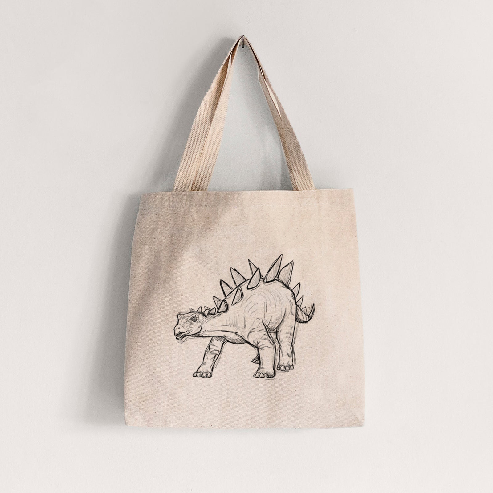 Natural canvas tote bag printed with a black ink illustration of a Stegosaurus with plates along its back.