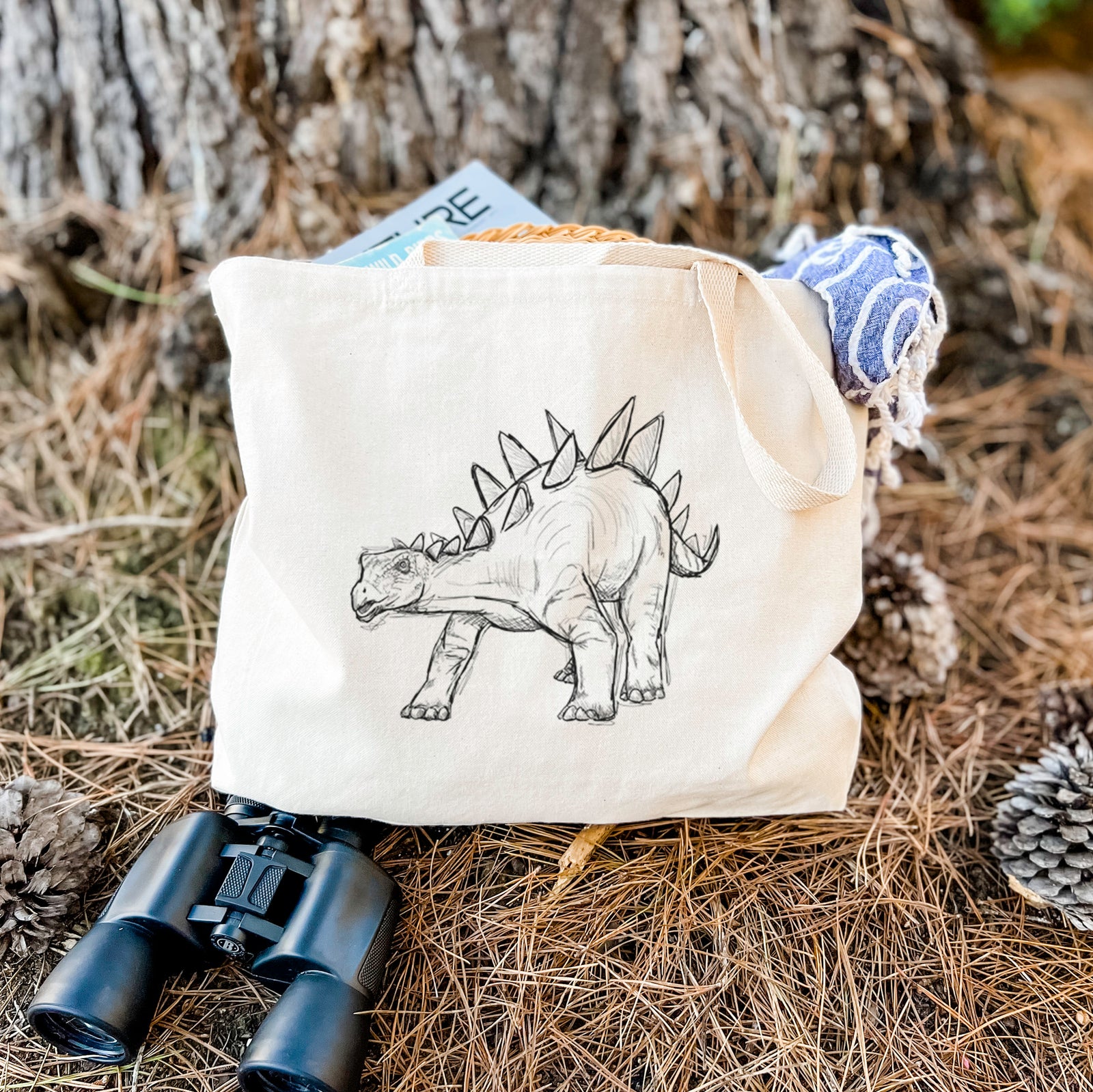 Natural canvas tote bag printed with a black ink illustration of a Stegosaurus with plates along its back.