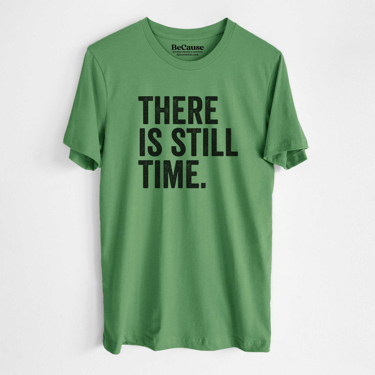 Leaf green lightweight cotton t-shirt laid flat, printed with bold black words reading There Is Still Time.