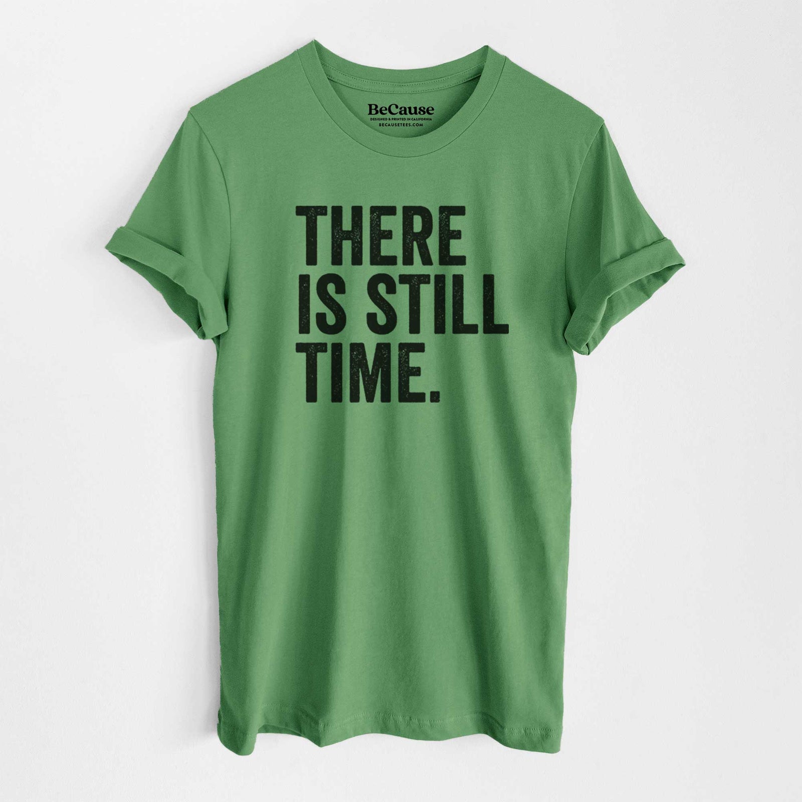 Leaf green lightweight cotton t-shirt laid flat, printed with bold black words reading There Is Still Time.