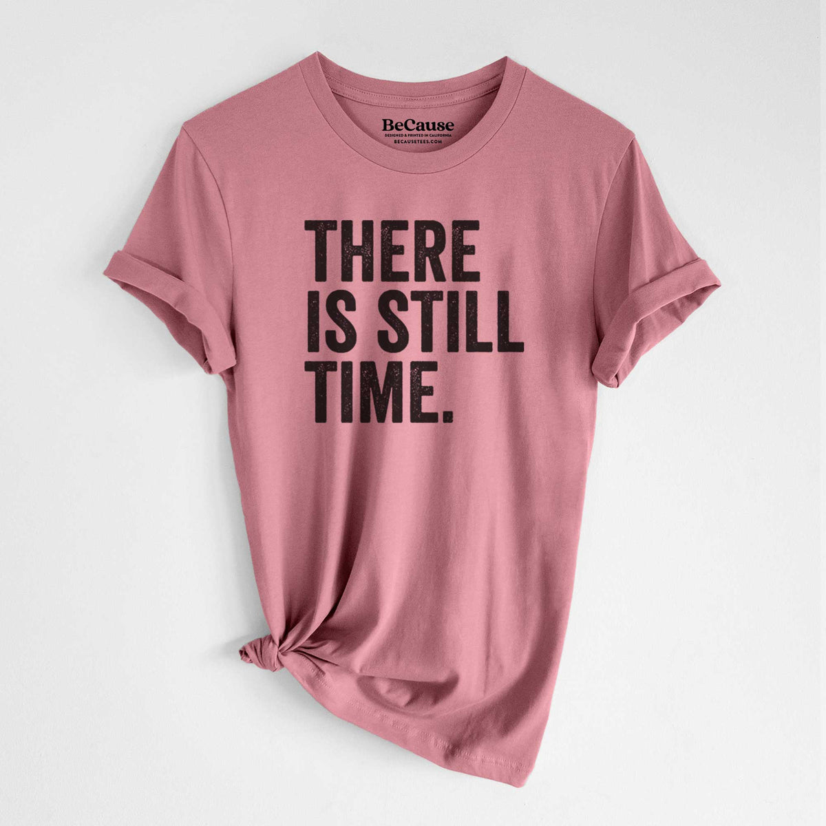 Mauve pink lightweight cotton t-shirt laid flat with the sleeves rolled, printed with bold black words reading There Is Still Time.