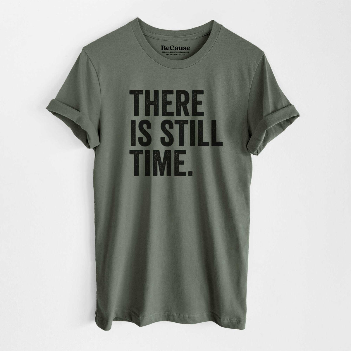 Military green lightweight cotton t-shirt laid flat, printed with bold black words reading There Is Still Time.