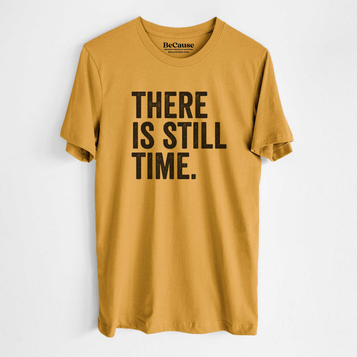 Mustard yellow lightweight cotton t-shirt laid flat, printed with bold black words reading There Is Still Time.