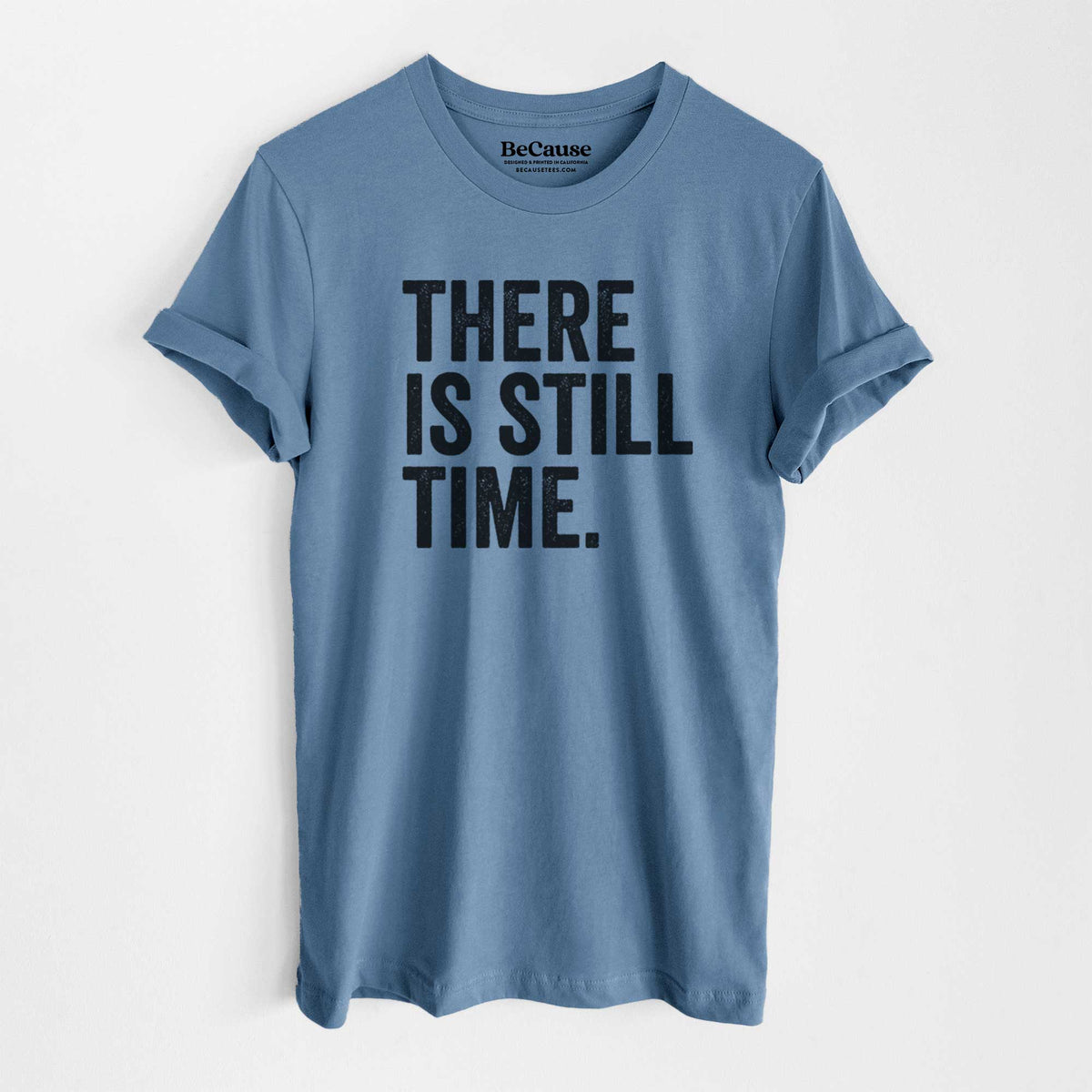 Steel blue lightweight cotton t-shirt laid flat, printed with bold black words reading There Is Still Time.