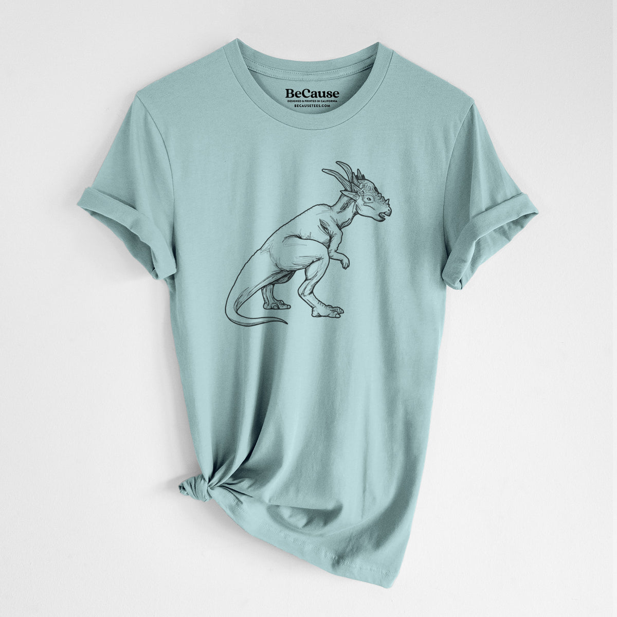 Dusty blue lightweight cotton t-shirt laid flat with the sleeves rolled, printed with a black ink illustration of a Stygimoloch dinosaur with a spiky domed head.