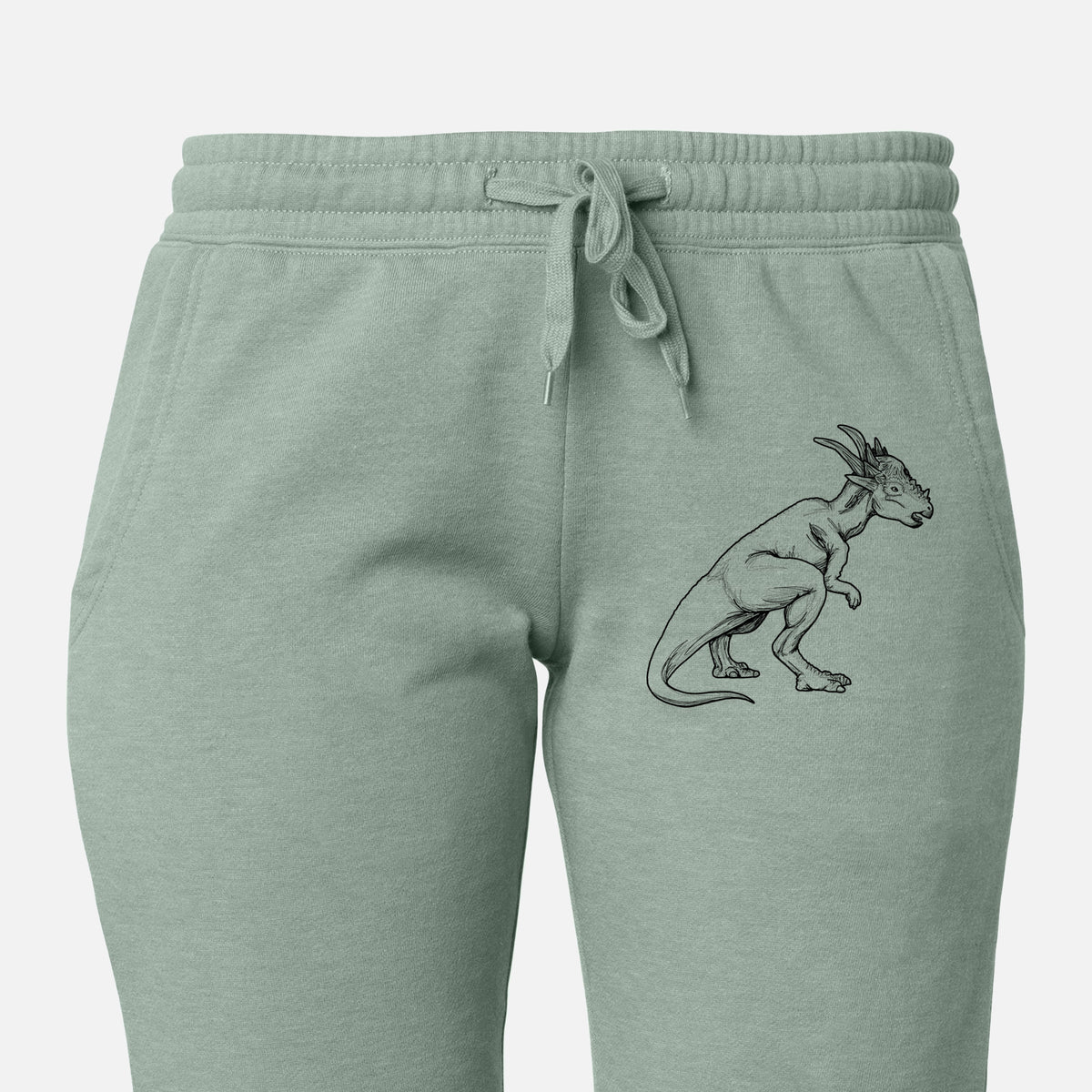 Front of sage green Cali Wave sweatpants, printed with a black ink illustration of a Stygimoloch dinosaur with a spiky domed head on the leg.