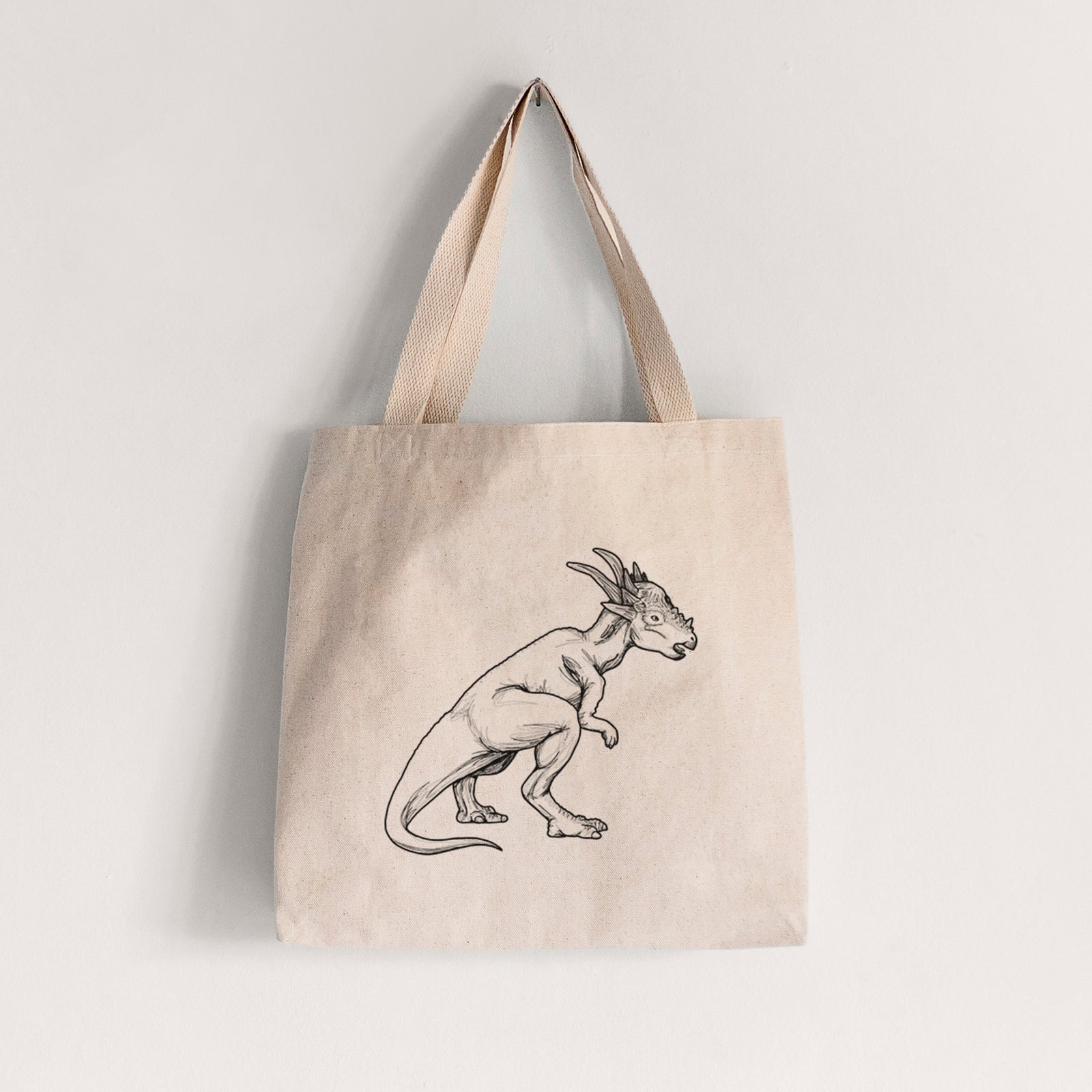 Natural canvas tote bag printed with a black ink illustration of a Stygimoloch dinosaur with a spiky domed head.