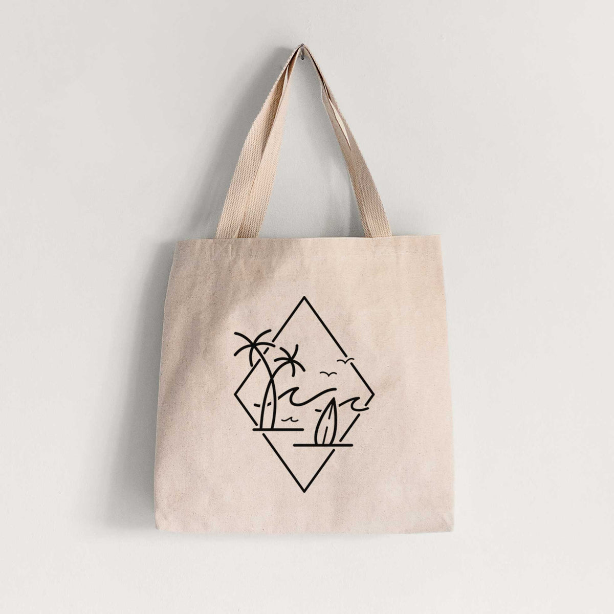 Natural canvas tote bag printed with black line art of palm trees, ocean waves, birds and a surfboard inside a diamond outline.