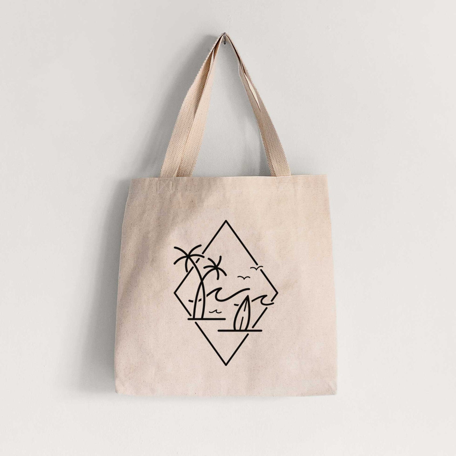 Natural canvas tote bag printed with black line art of palm trees, ocean waves, birds and a surfboard inside a diamond outline.
