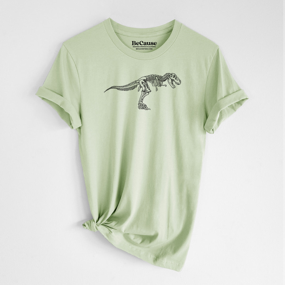 Spring green lightweight cotton t-shirt laid flat with the sleeves rolled, printed with a black ink illustration of a Tyrannosaurus rex skeleton.