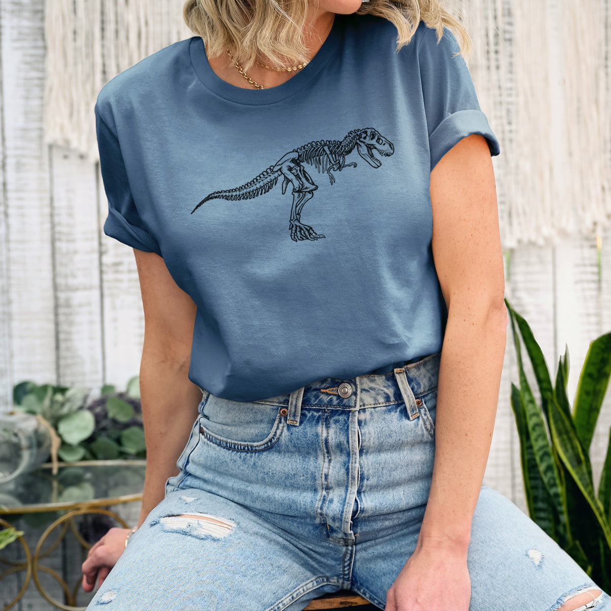 Woman wearing a steel blue lightweight cotton t-shirt printed with a black ink illustration of a Tyrannosaurus rex skeleton.