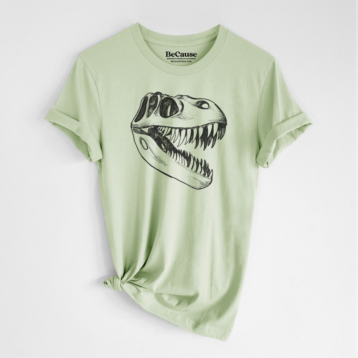 Spring green lightweight cotton t-shirt laid flat with the sleeves rolled, printed with a black ink illustration of a Tyrannosaurus rex skull with sharp teeth.