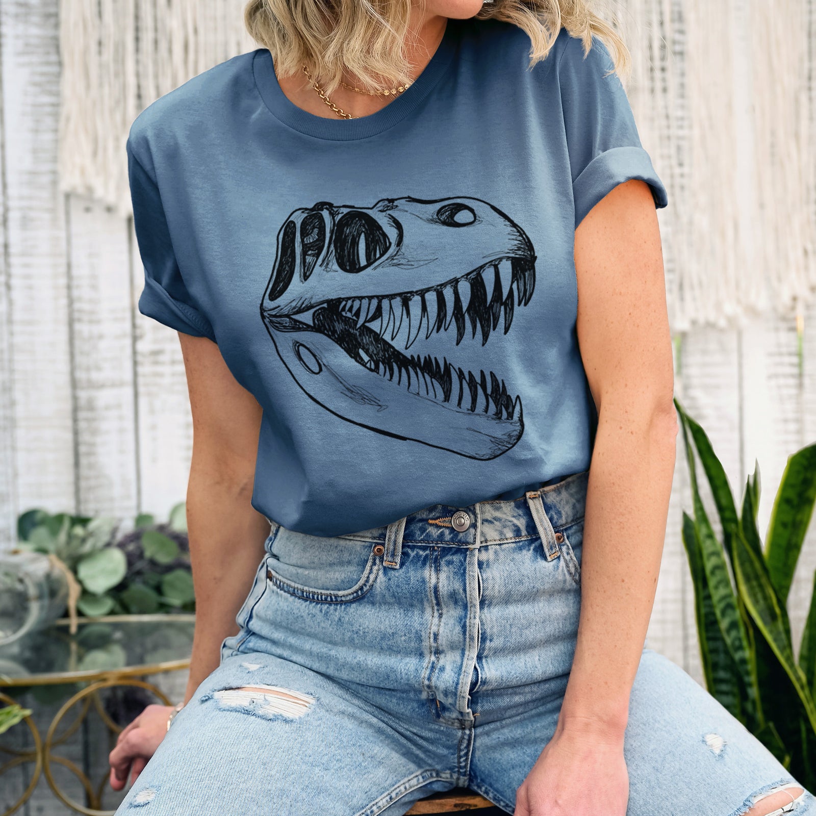 Autumn lightweight cotton t-shirt laid flat, printed with a black ink illustration of a Tyrannosaurus rex skull with sharp teeth.