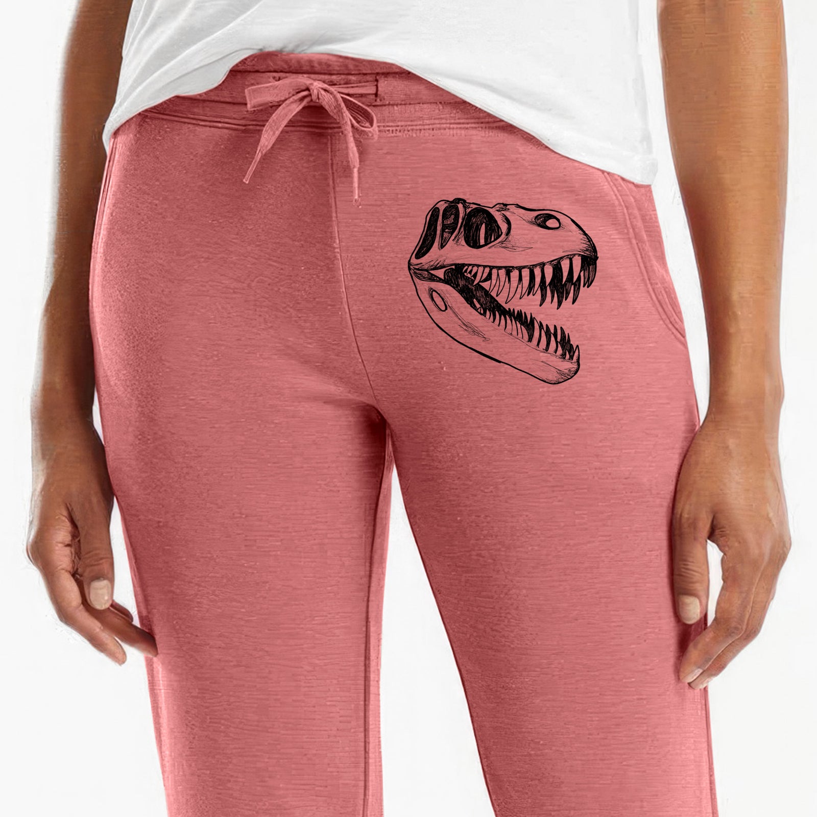 Front of dusty rose Cali Wave sweatpants, printed with a black ink illustration of a Tyrannosaurus rex skull with sharp teeth on the leg.