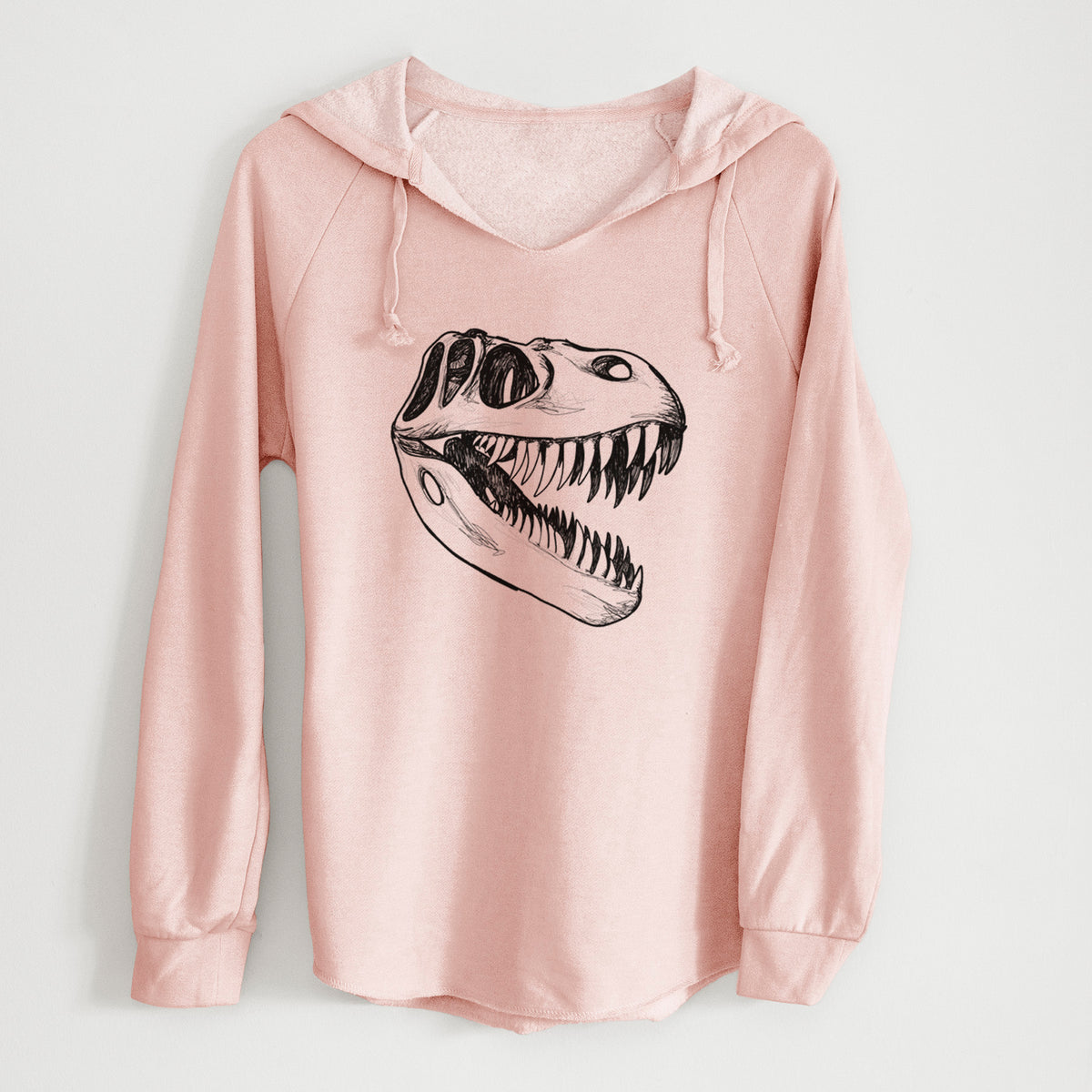 Blush pink women's Cali Wave hooded sweatshirt laid flat, printed with a black ink illustration of a Tyrannosaurus rex skull with sharp teeth.