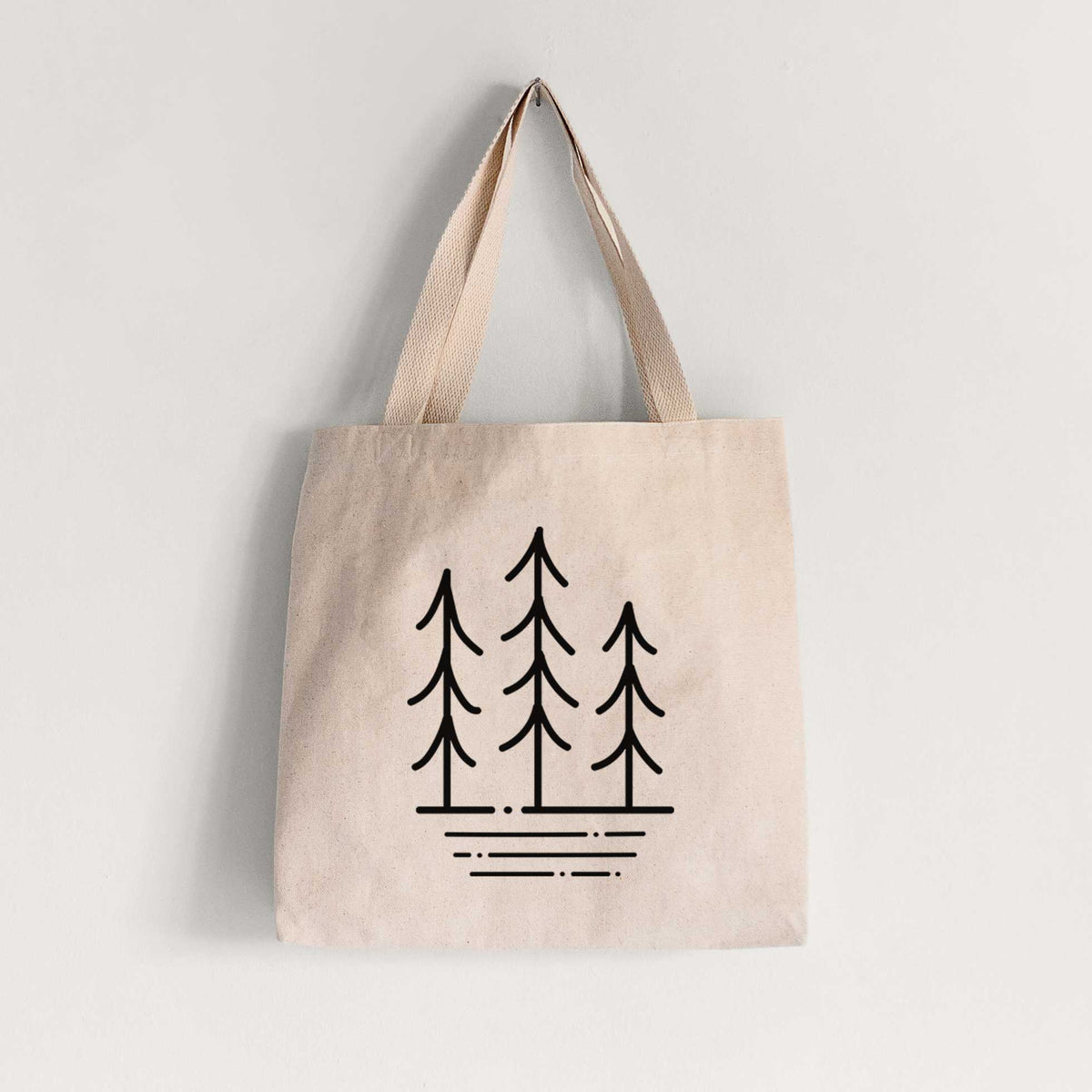 Natural canvas tote bag printed with black line art of three simple pine trees above horizontal lines.