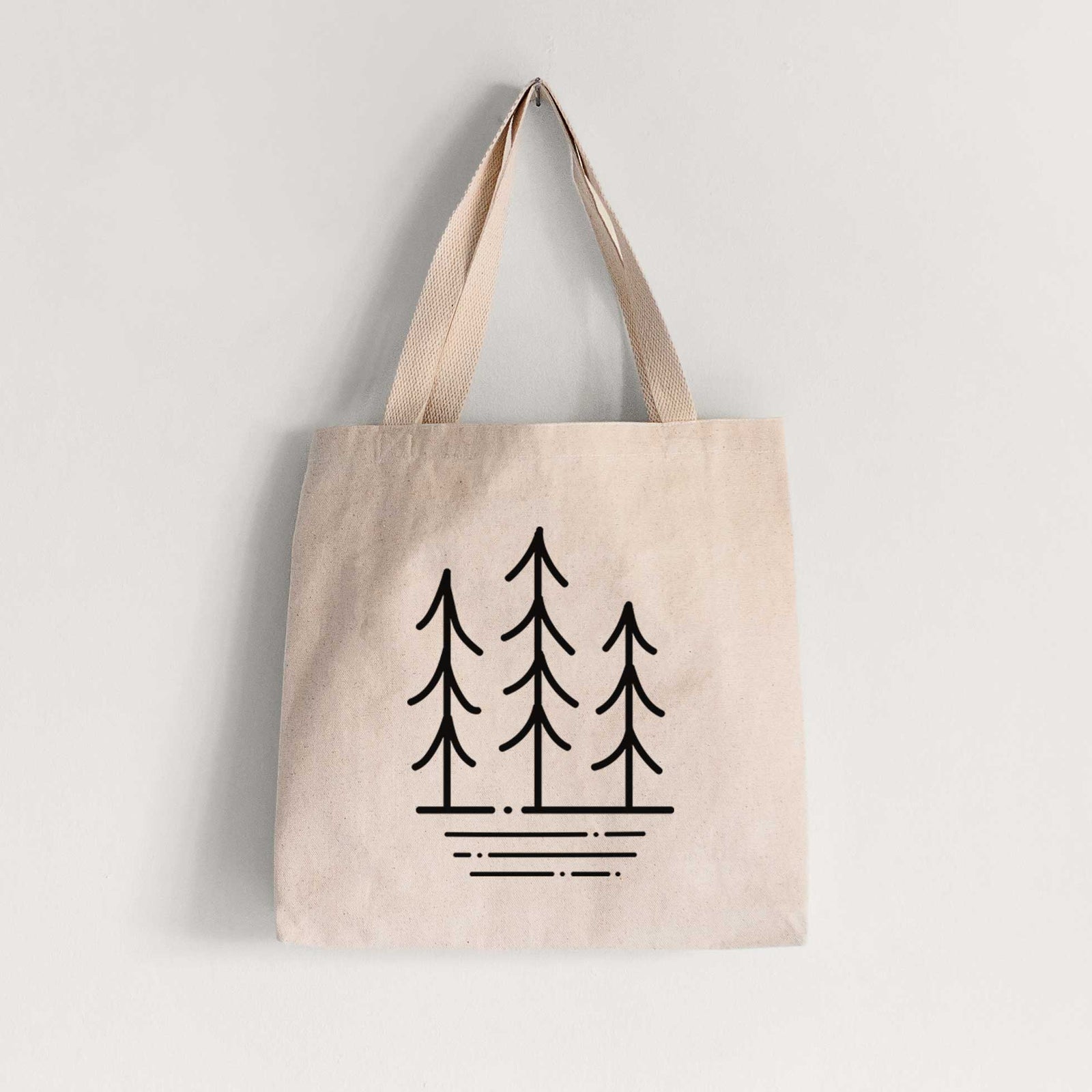 Natural canvas tote bag printed with black line art of three simple pine trees above horizontal lines.