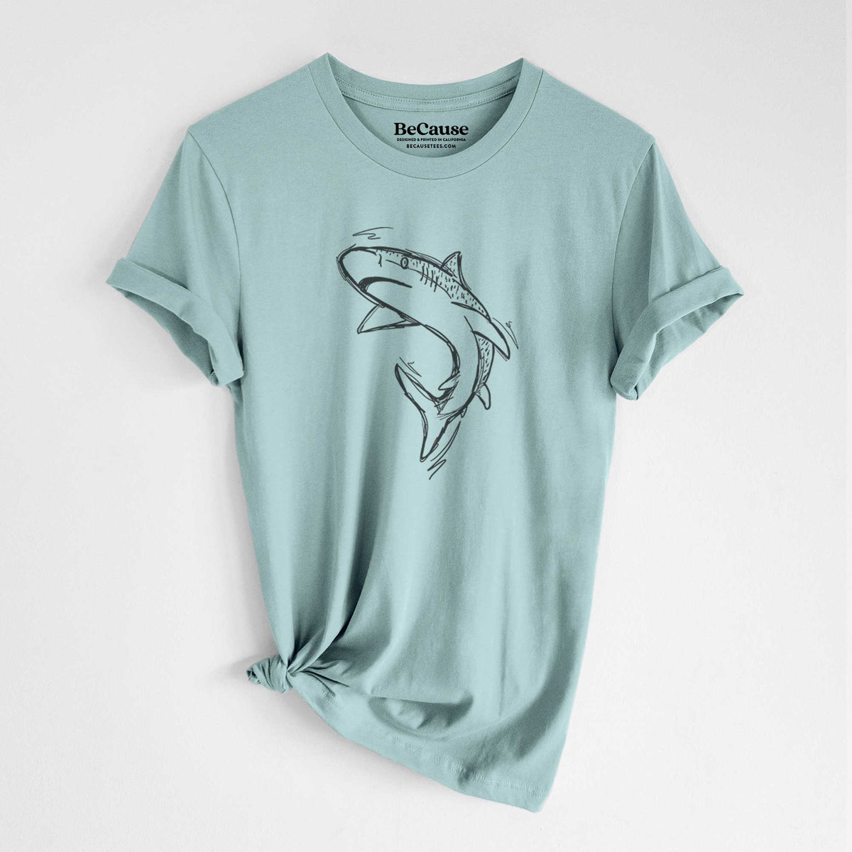 Dusty blue lightweight cotton t-shirt laid flat with the sleeves rolled, printed with a black ink illustration of a tiger shark swimming in a curve.