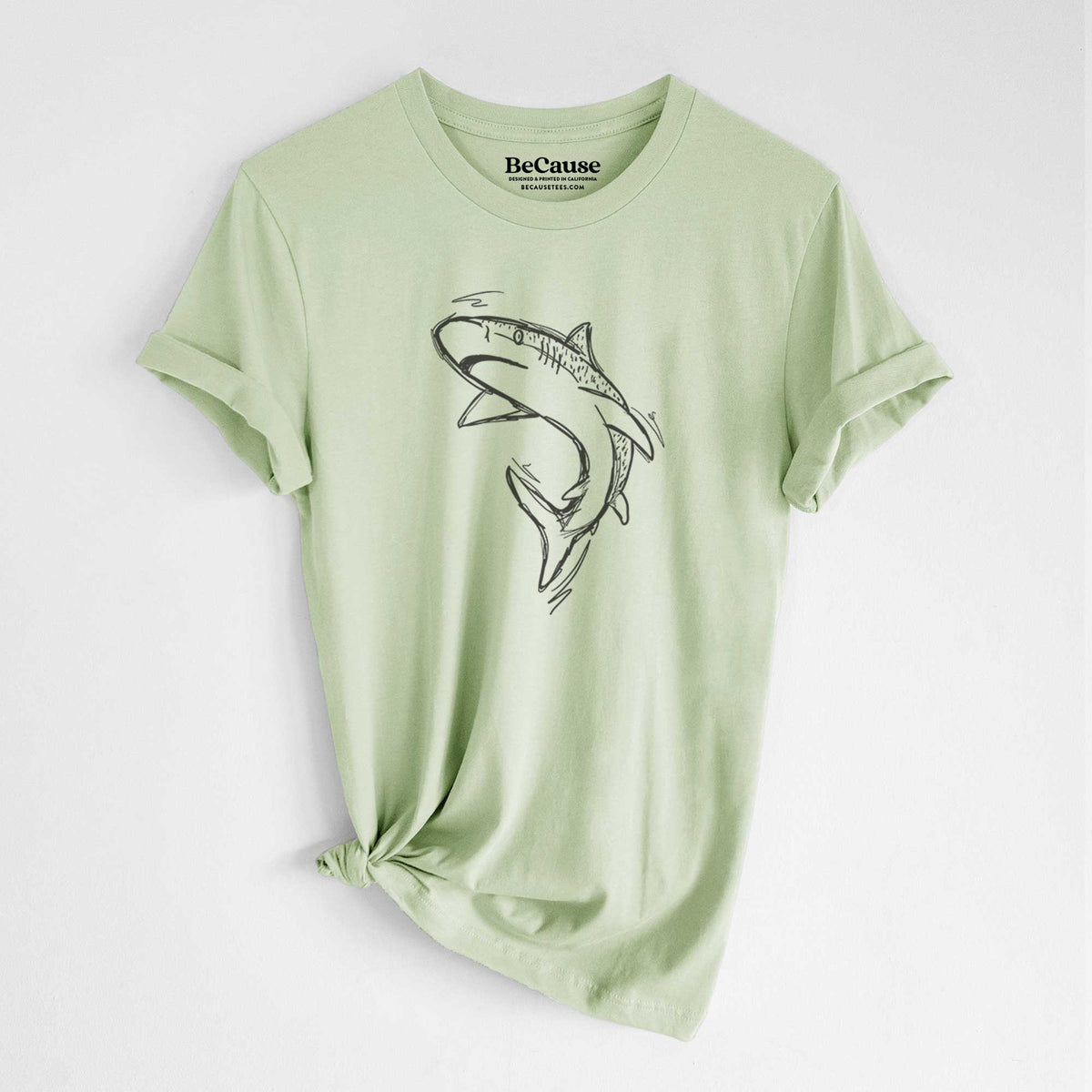 Spring green lightweight cotton t-shirt laid flat with the sleeves rolled, printed with a black ink illustration of a tiger shark swimming in a curve.