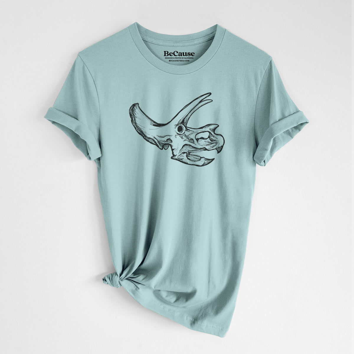 Dusty blue lightweight cotton t-shirt laid flat with the sleeves rolled, printed with a detailed black ink illustration of a Triceratops skull with its horns and frill.