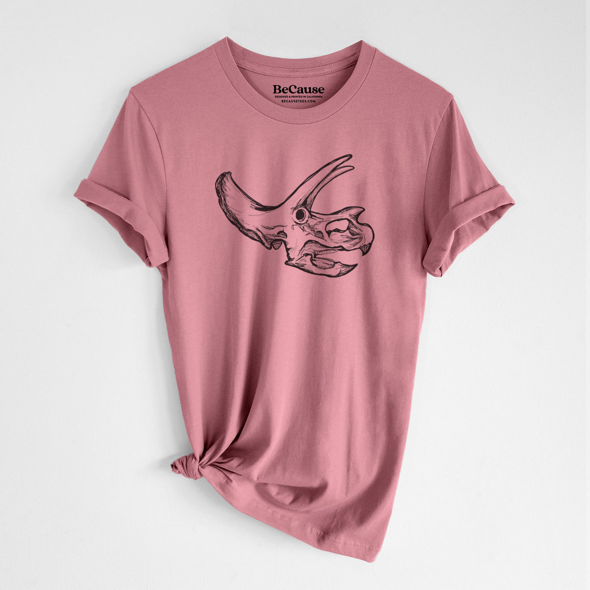Mauve pink lightweight cotton t-shirt laid flat with the sleeves rolled, printed with a detailed black ink illustration of a Triceratops skull with its horns and frill.