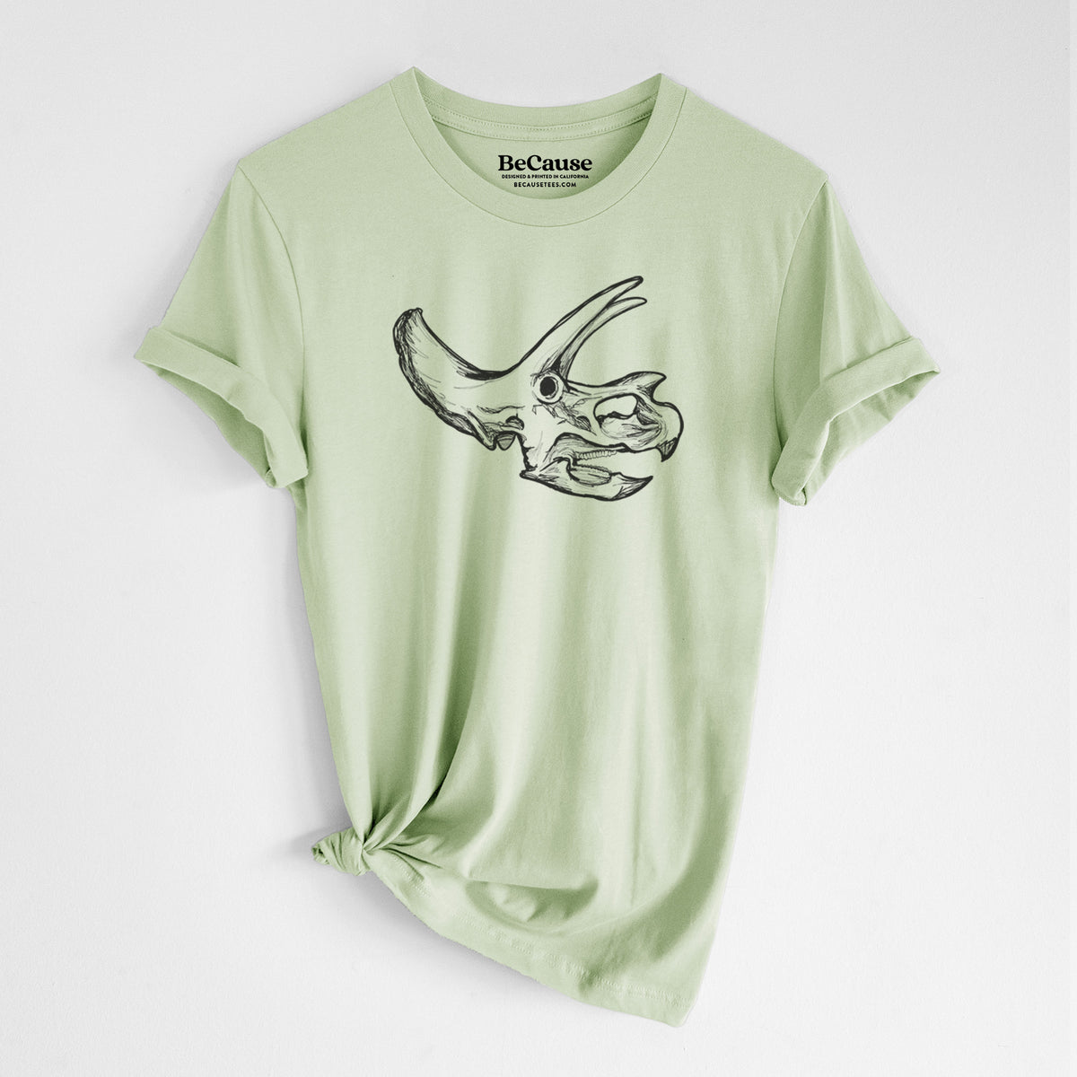 Spring green lightweight cotton t-shirt laid flat with the sleeves rolled, printed with a detailed black ink illustration of a Triceratops skull with its horns and frill.