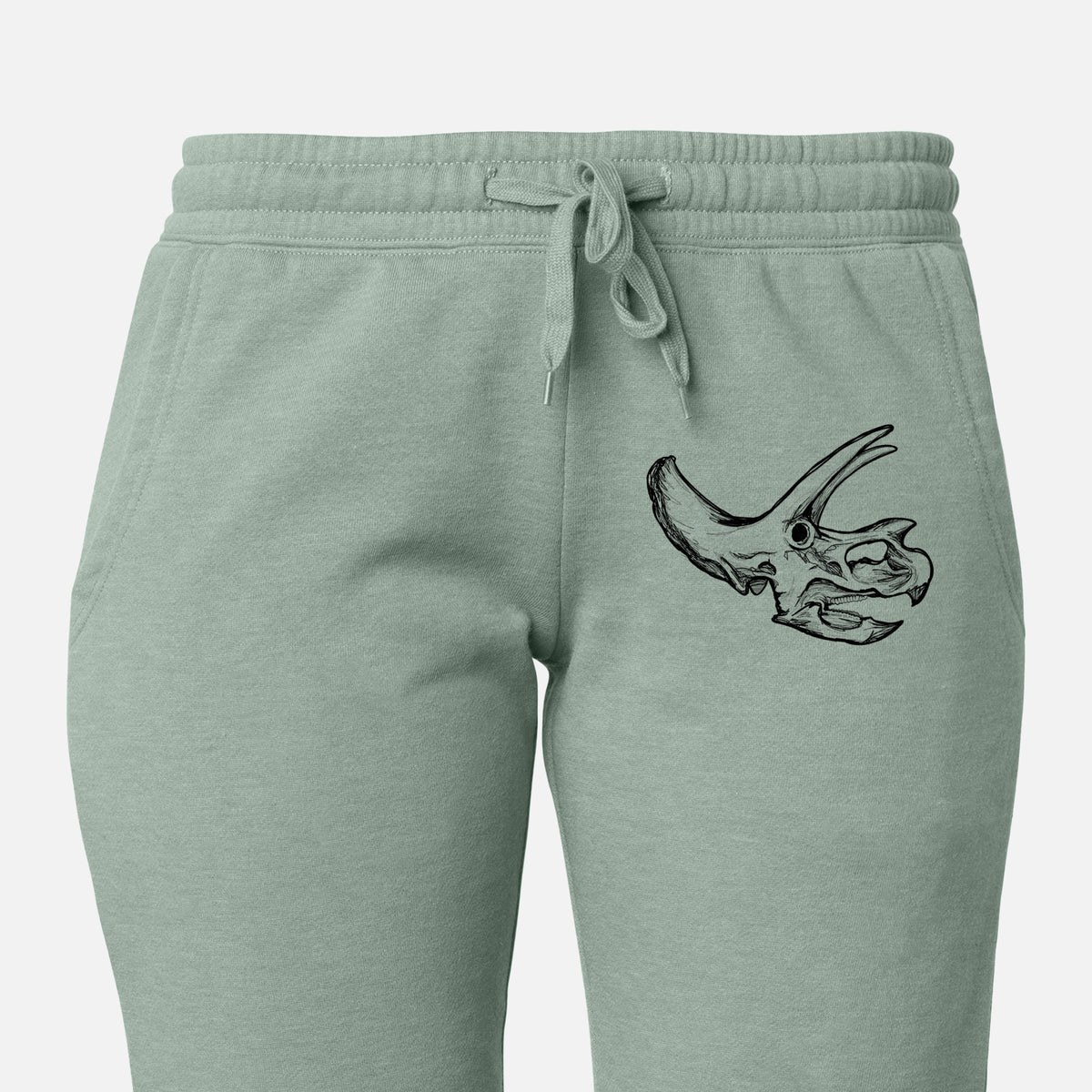 Front of sage green Cali Wave sweatpants, printed with a detailed black ink illustration of a Triceratops skull with its horns and frill on the leg.