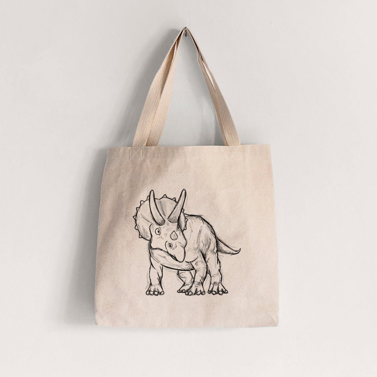 Natural canvas tote bag printed with a black ink illustration of a Triceratops walking.