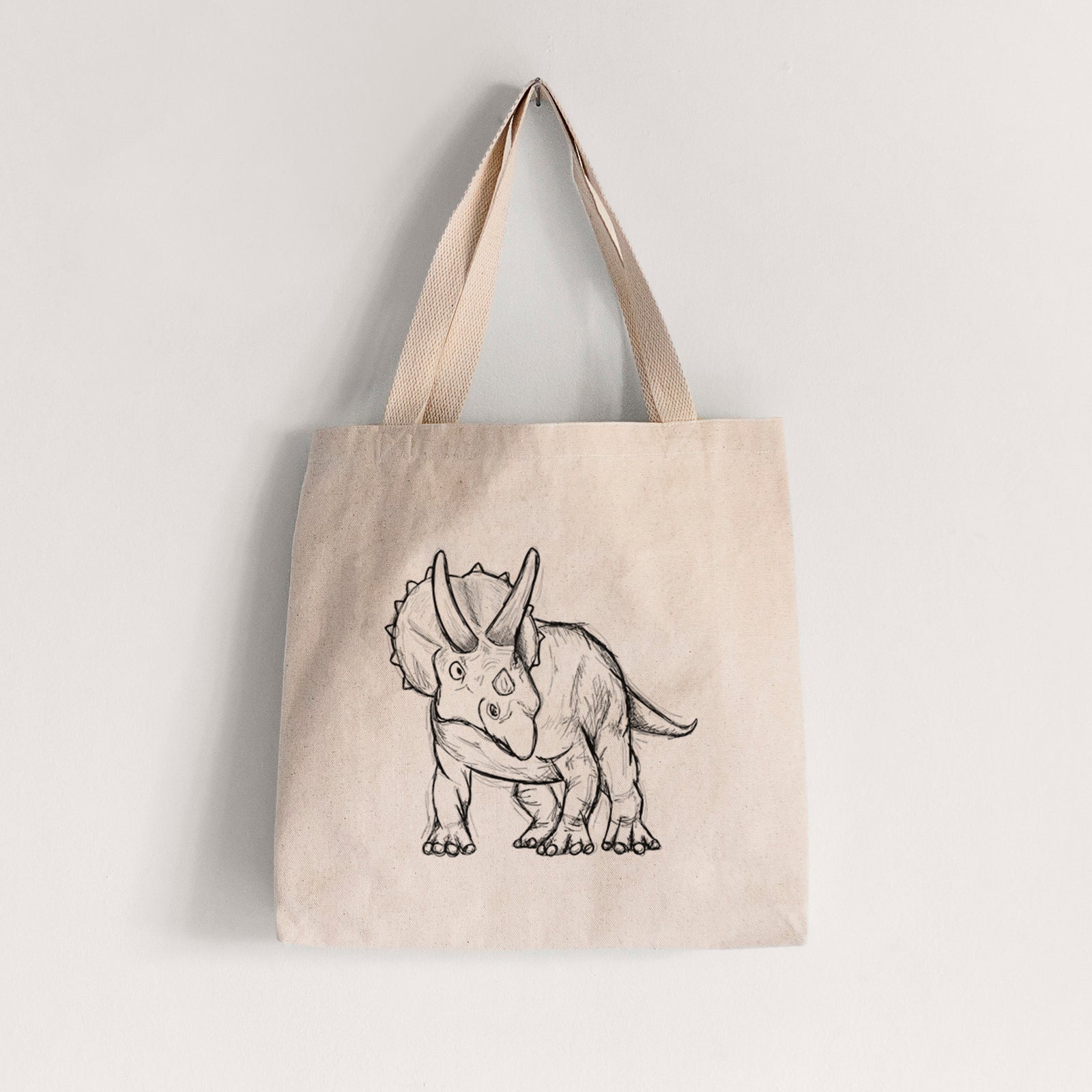 Natural canvas tote bag printed with a black ink illustration of a Triceratops walking.
