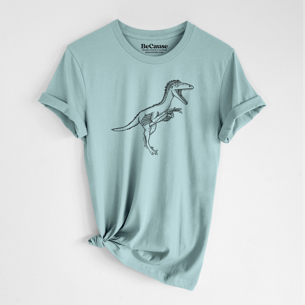 Dusty blue lightweight cotton t-shirt laid flat with the sleeves rolled, printed with a black ink illustration of a Troodon dinosaur running.