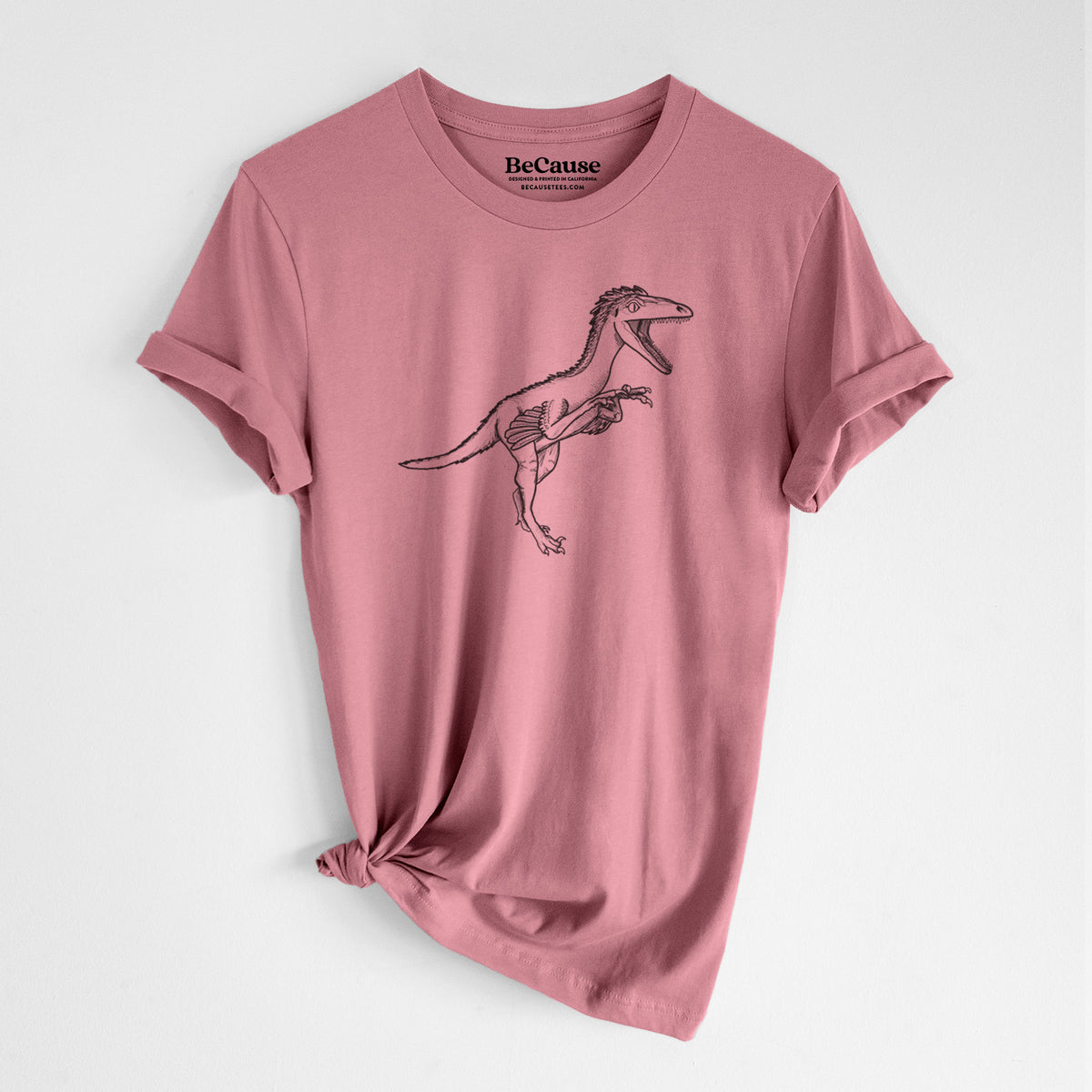 Mauve pink lightweight cotton t-shirt laid flat with the sleeves rolled, printed with a black ink illustration of a Troodon dinosaur running.