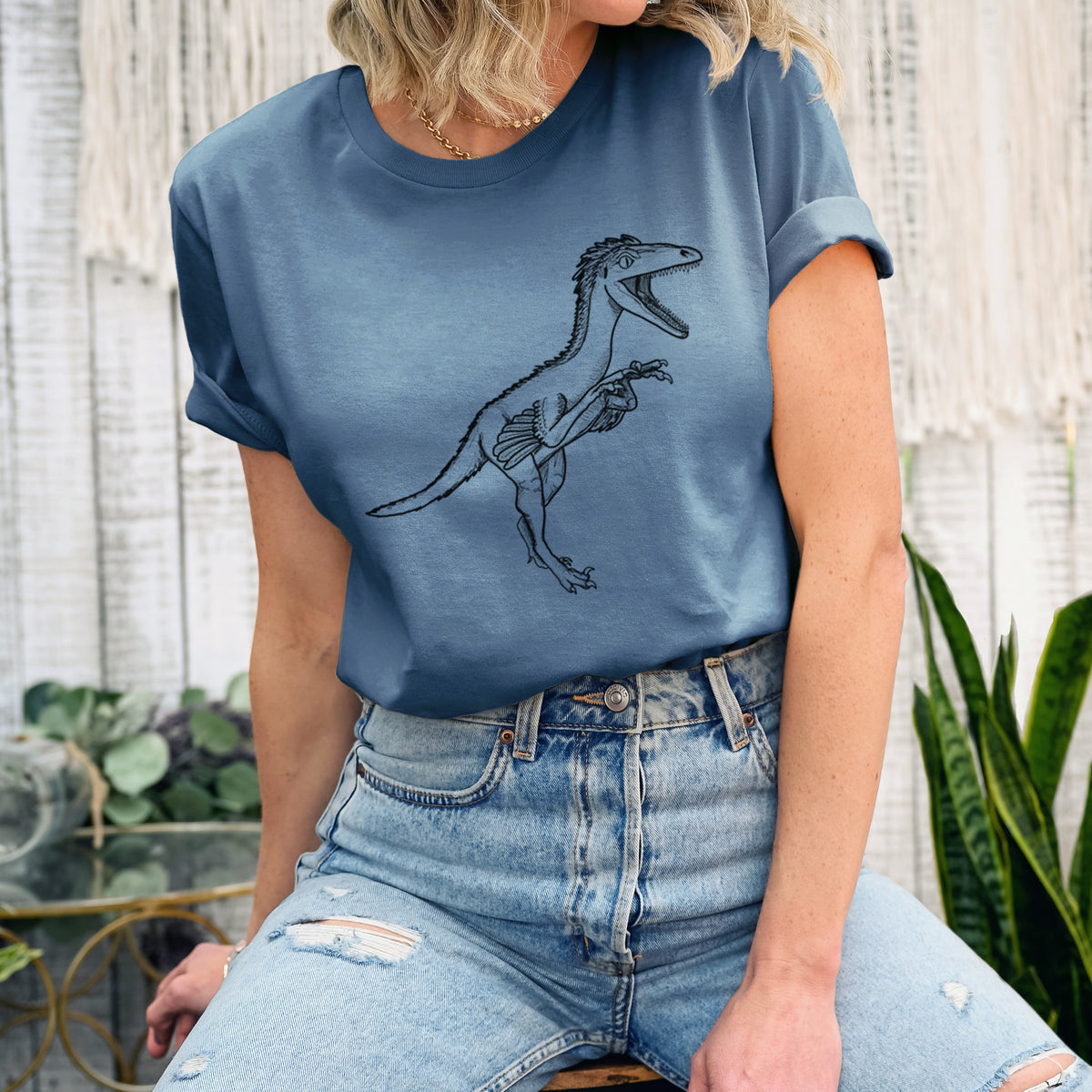 Woman wearing a steel blue lightweight cotton t-shirt printed with a black ink illustration of a Troodon dinosaur running.