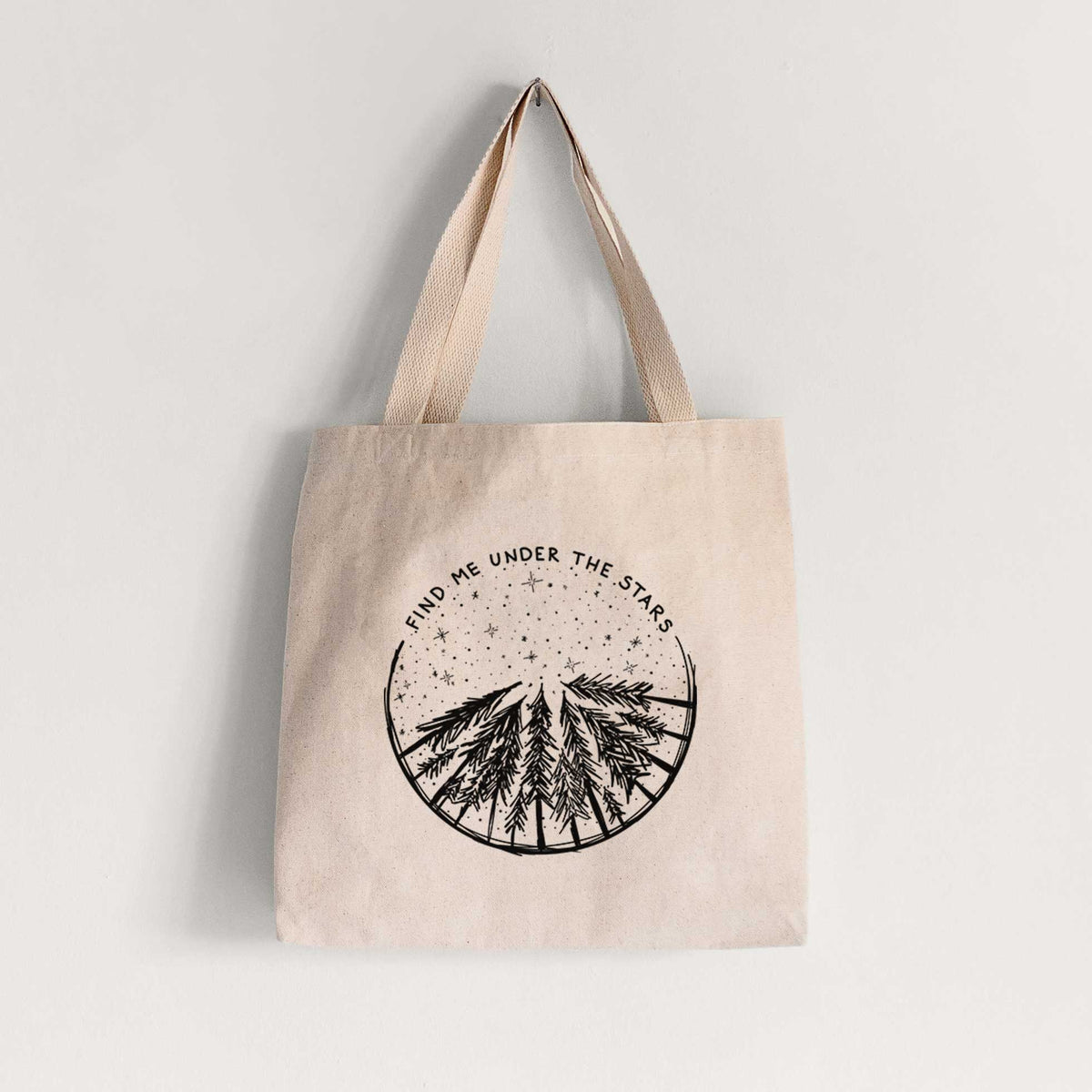 Natural canvas tote bag printed with a circle of pine trees under a starry sky, with the words Find Me Under the Stars.