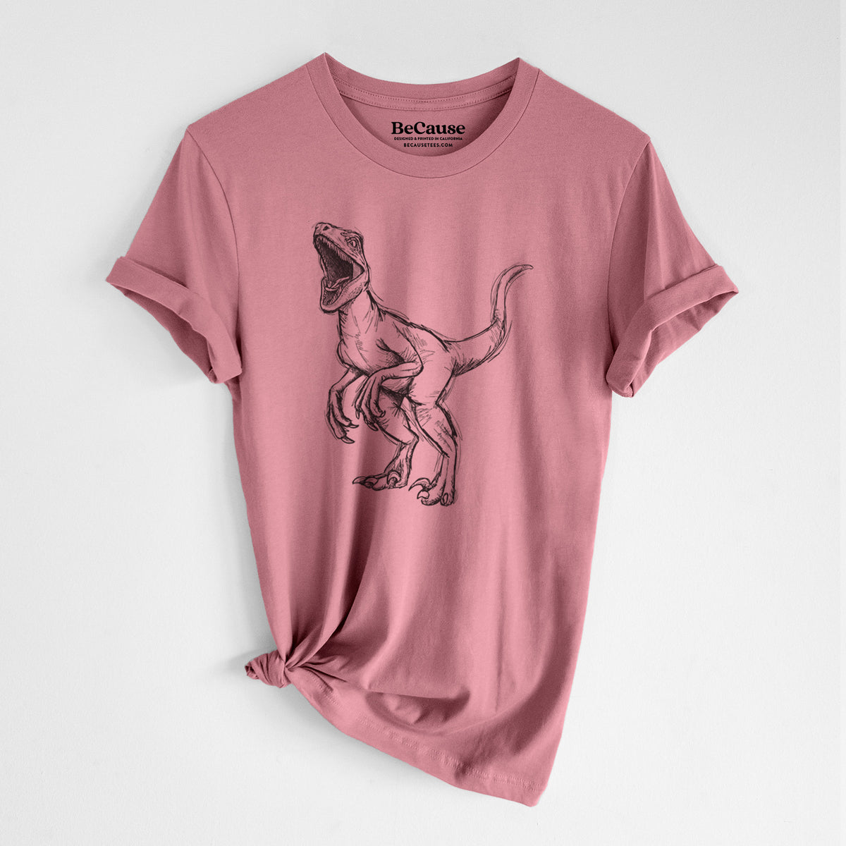 Mauve pink lightweight cotton t-shirt laid flat with the sleeves rolled, printed with a black ink illustration of a Velociraptor roaring.