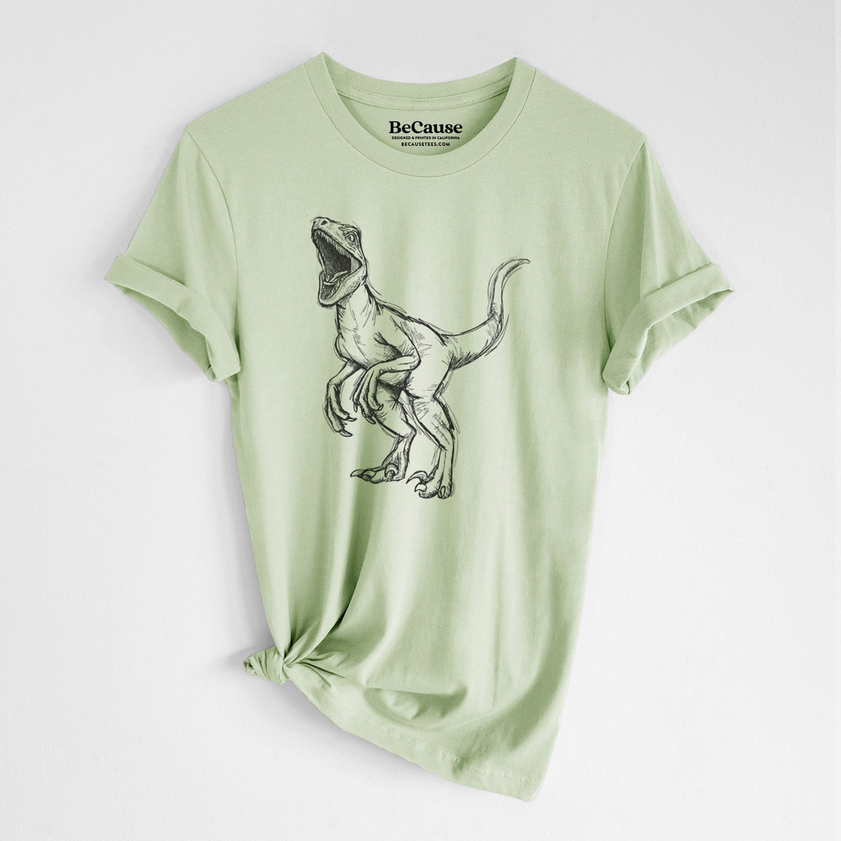 Spring green lightweight cotton t-shirt laid flat with the sleeves rolled, printed with a black ink illustration of a Velociraptor roaring.