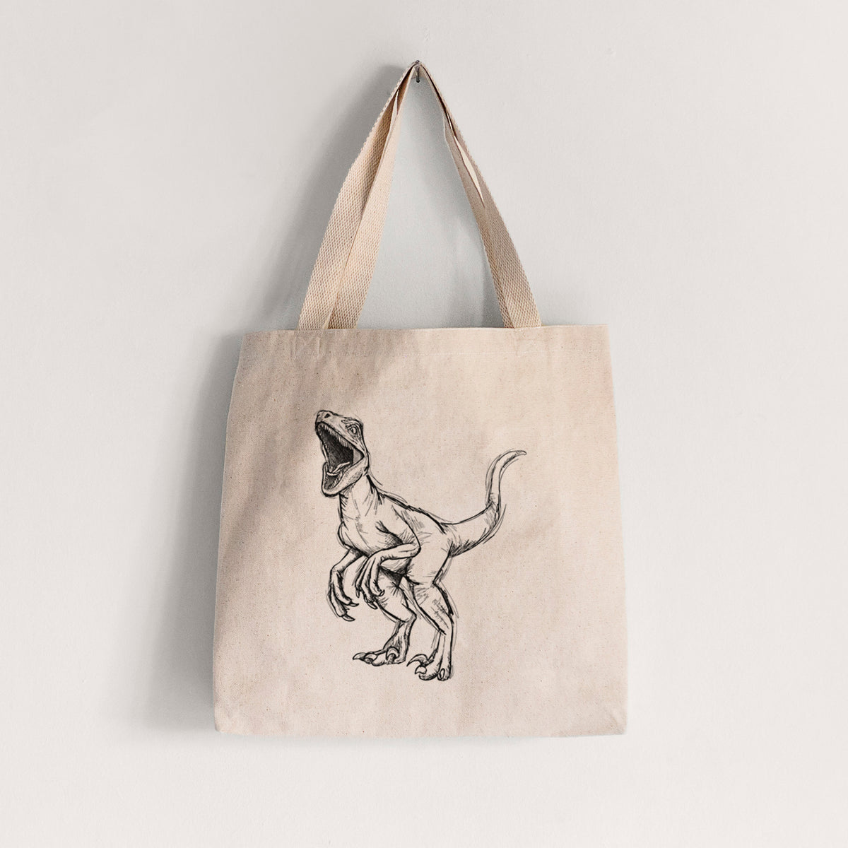 Natural canvas tote bag printed with a black ink illustration of a Velociraptor roaring.
