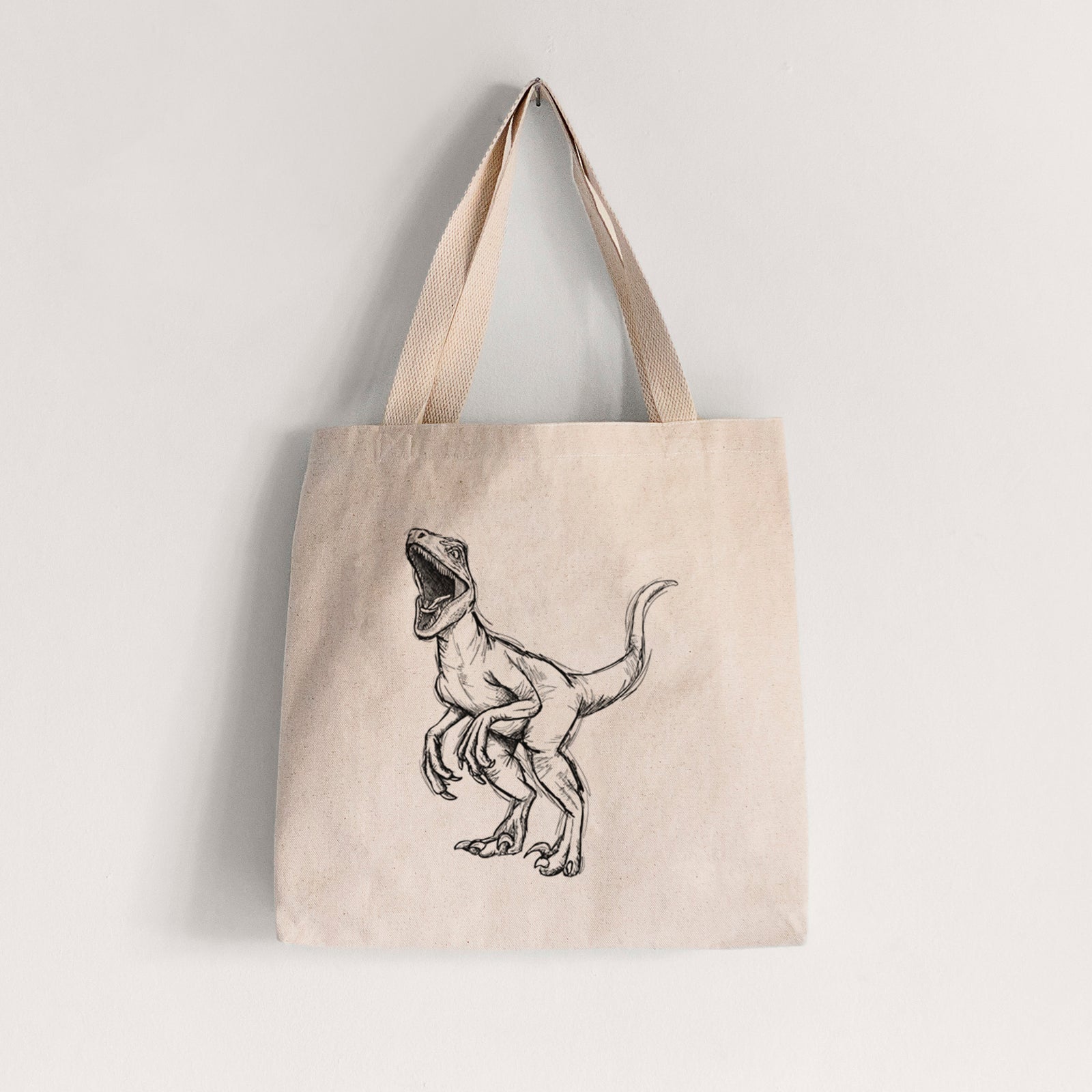 Natural canvas tote bag printed with a black ink illustration of a Velociraptor roaring.