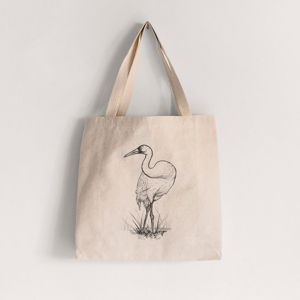 Natural canvas tote bag printed with a detailed black ink illustration of a whooping crane standing in grass.