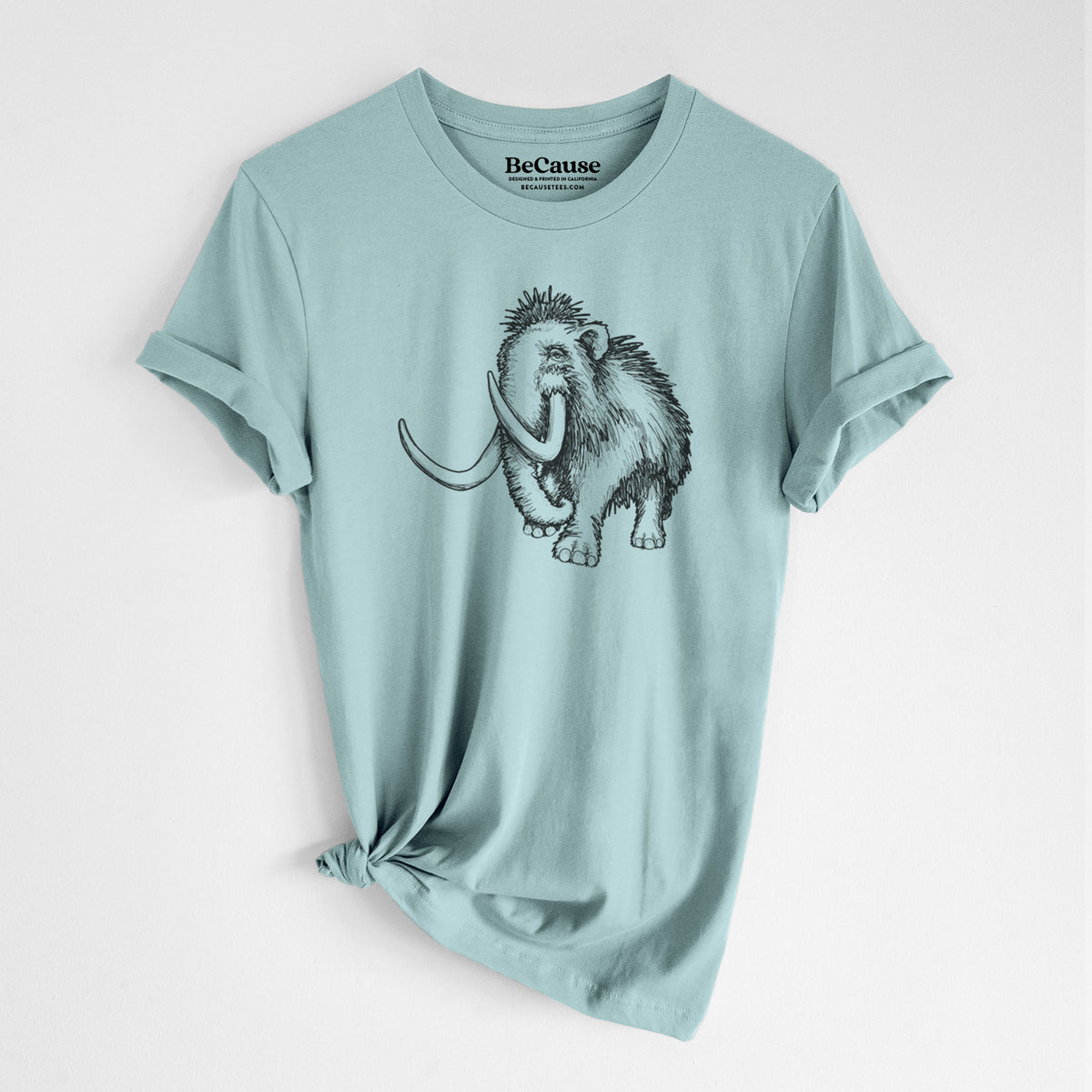 Dusty blue lightweight cotton t-shirt laid flat with the sleeves rolled, printed with a black ink illustration of a woolly mammoth with long curved tusks.