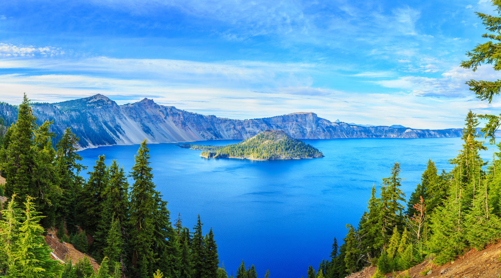 Scenic view of Crater Lake with Wizard Island and pine trees under a blue sky, showing what to expect when to visit Crater Lake.