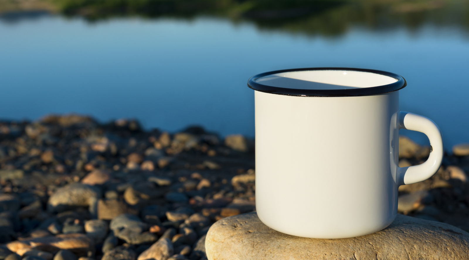 plastic free outdoor dishes: an enamel mug sits on a rock by blue water