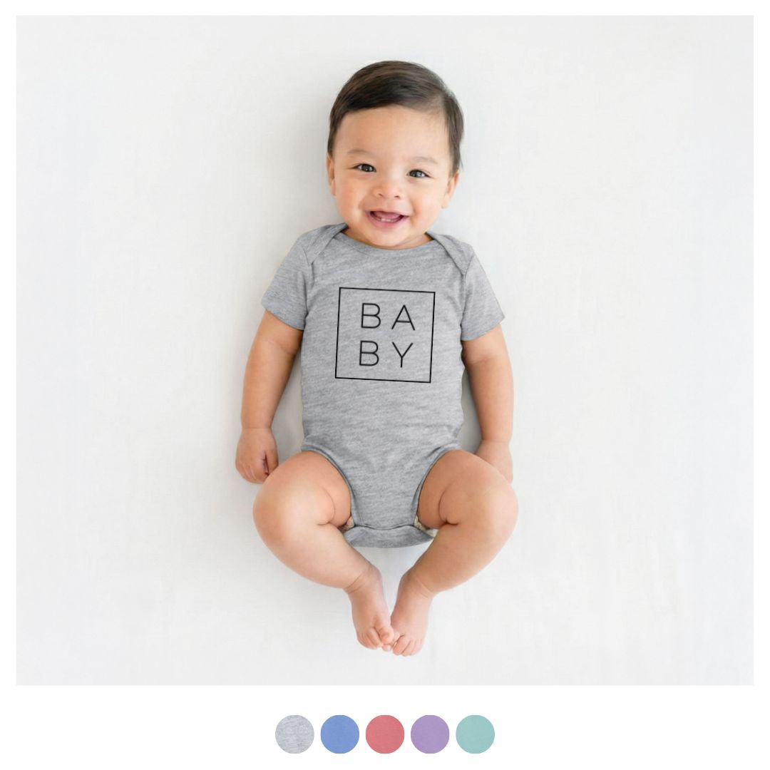 Smiling baby wearing a heather grey fine jersey bodysuit with boxed "BABY" text art, featuring color swatches.