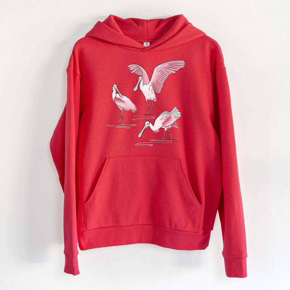 Roseate Spoonbill Trio - Platalea ajaja - Statement Midweight Hoodie in Cherry Red, hanging on a white wall, with a front kangaroo pocket and no drawcords.